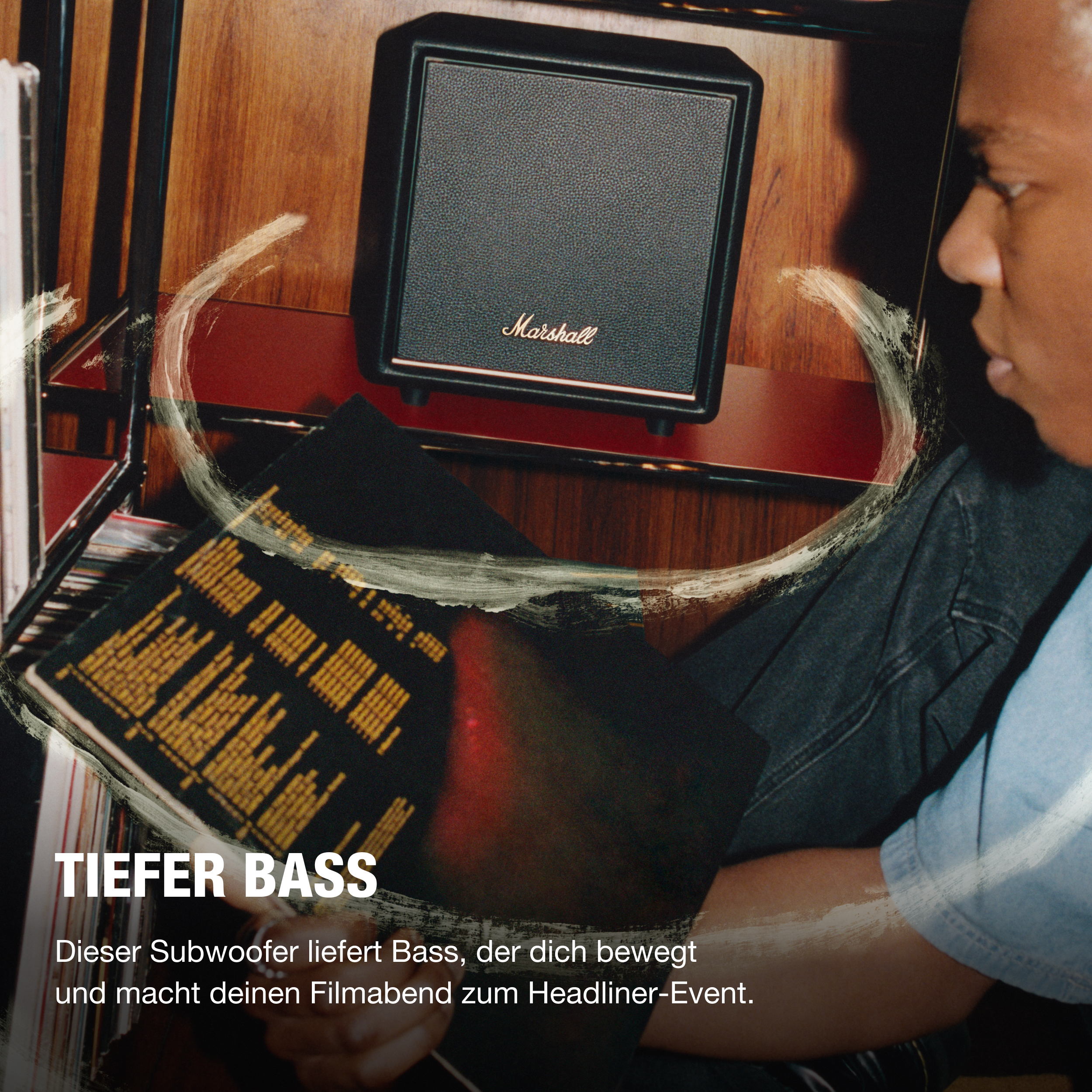 Eine Person sitzt in der Nähe eines Marshall-Lautsprechers. Text sagt 'TIEFER BASS'. Der Lautsprecher ist schwarz mit goldenem Logo.