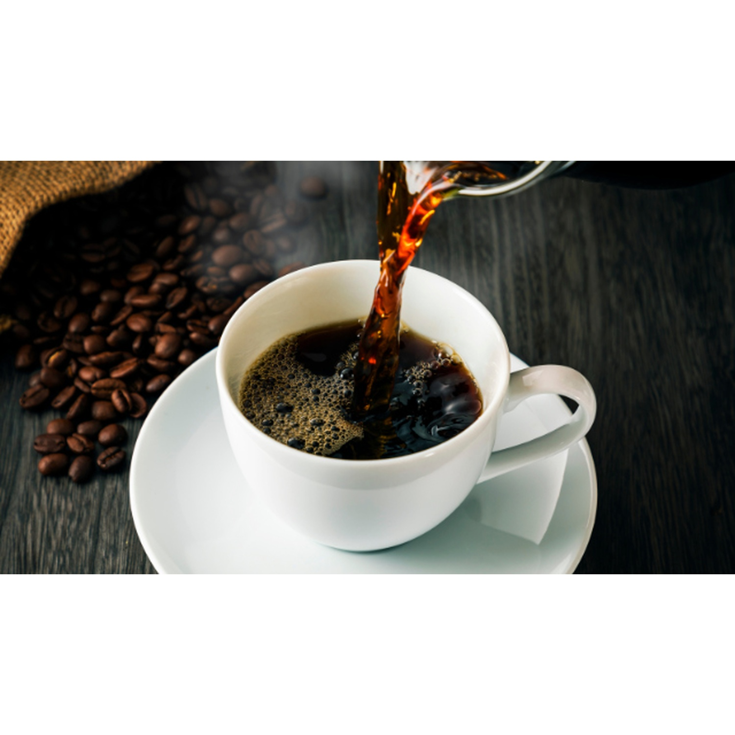 Caffè versato in una tazza bianca su un piattino. Chicchi di caffè e sacco di iuta sullo sfondo. Tavolo di legno scuro.