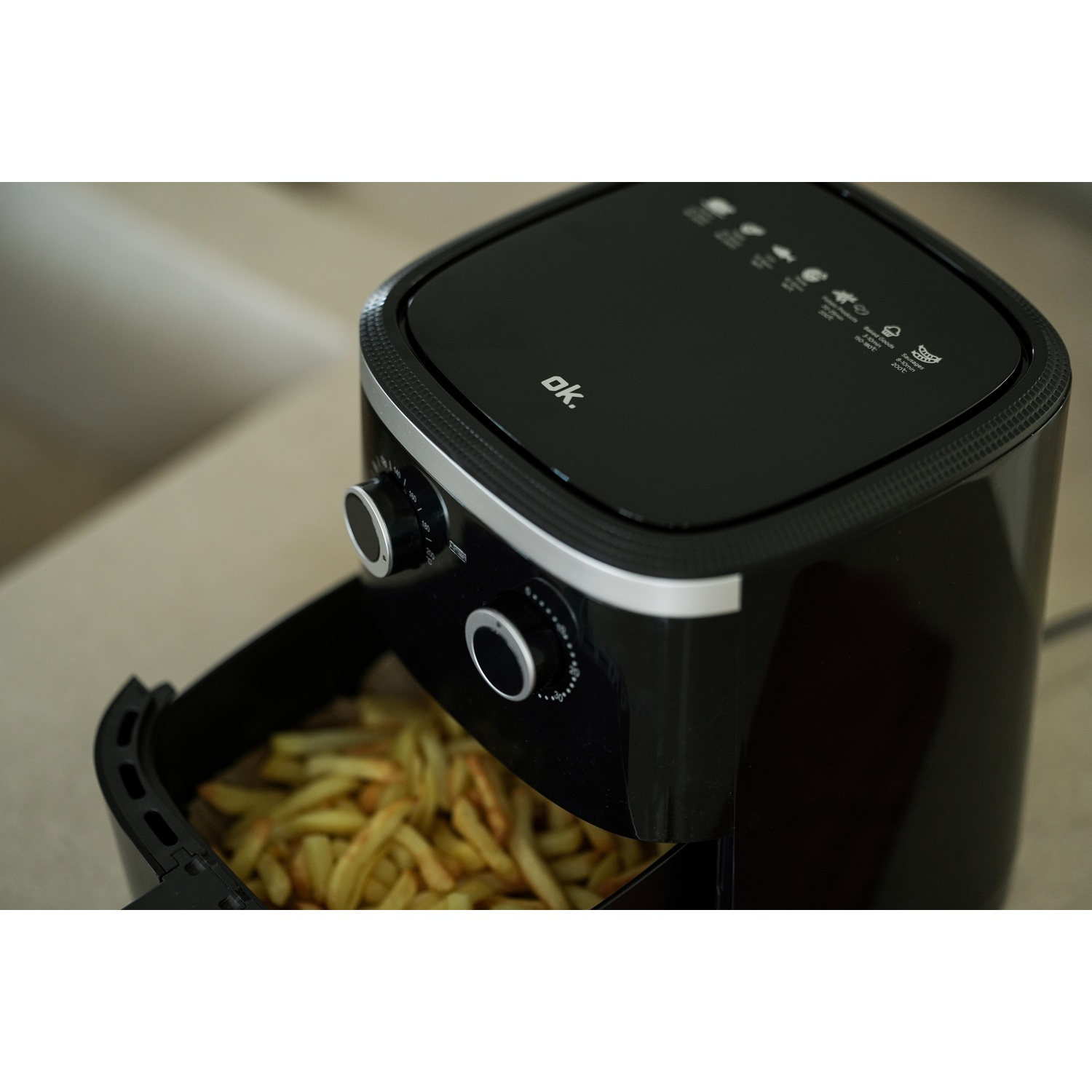 Friggitrice ad aria nera con cassetto pieno di patatine fritte. I comandi sono sul davanti. La parte superiore ha simboli di cottura. Logo 'ok.' visibile.