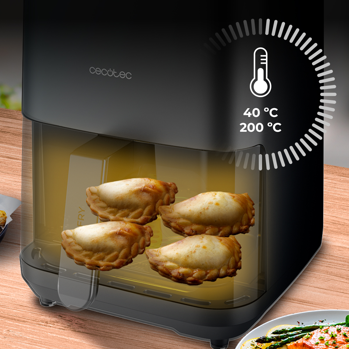 Una freidora de aire con cuatro empanadas doradas dentro. Un termómetro muestra 40°C y 200°C. El fondo es una mesa de madera.