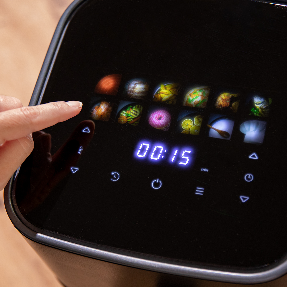 Una mano presiona un botón en una freidora de aire negra. La pantalla muestra 00:15. Hay iconos de comida encima de la pantalla.