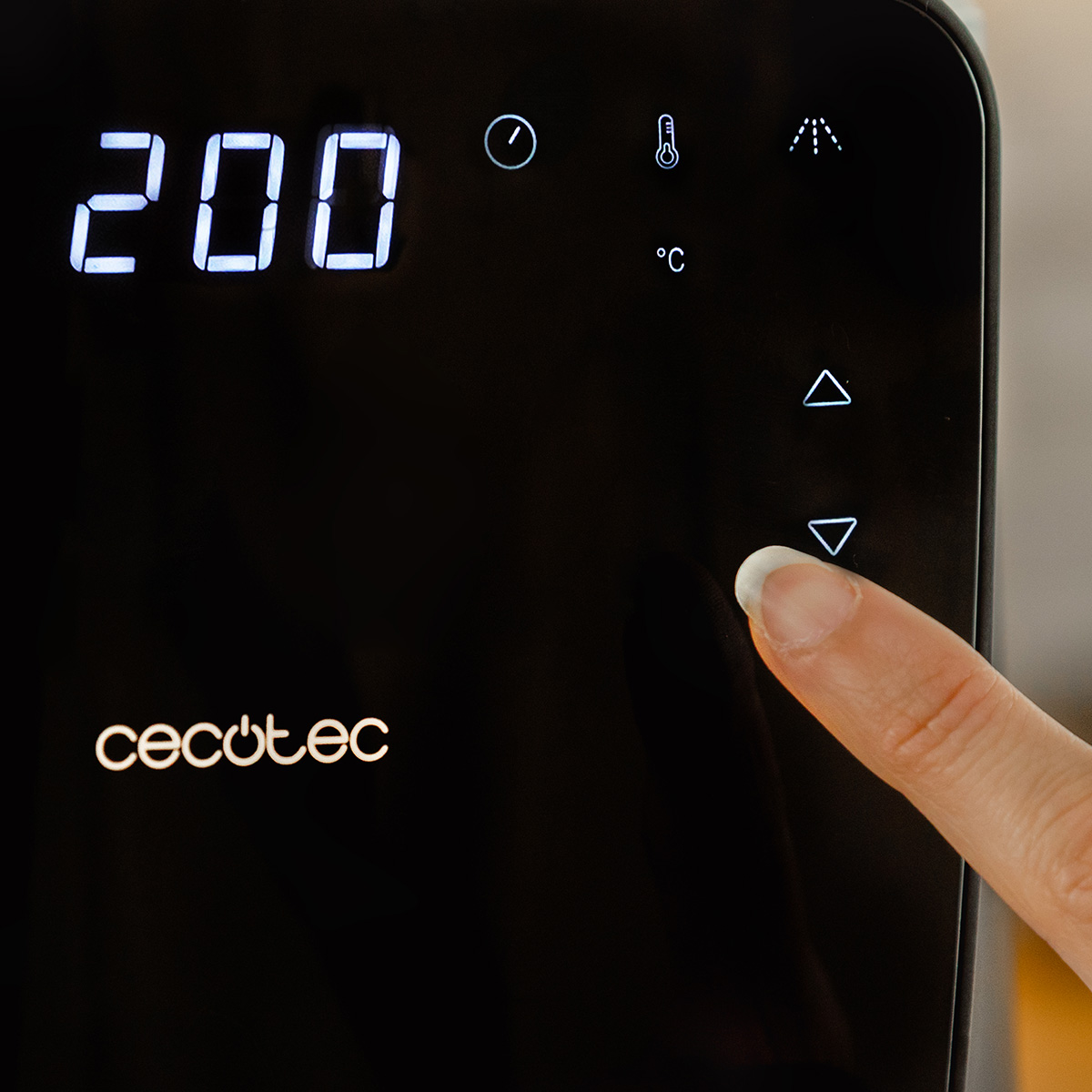 Una mano presiona la flecha hacia abajo en un panel negro de electrodomésticos. La pantalla muestra 200. Logos e iconos visibles.