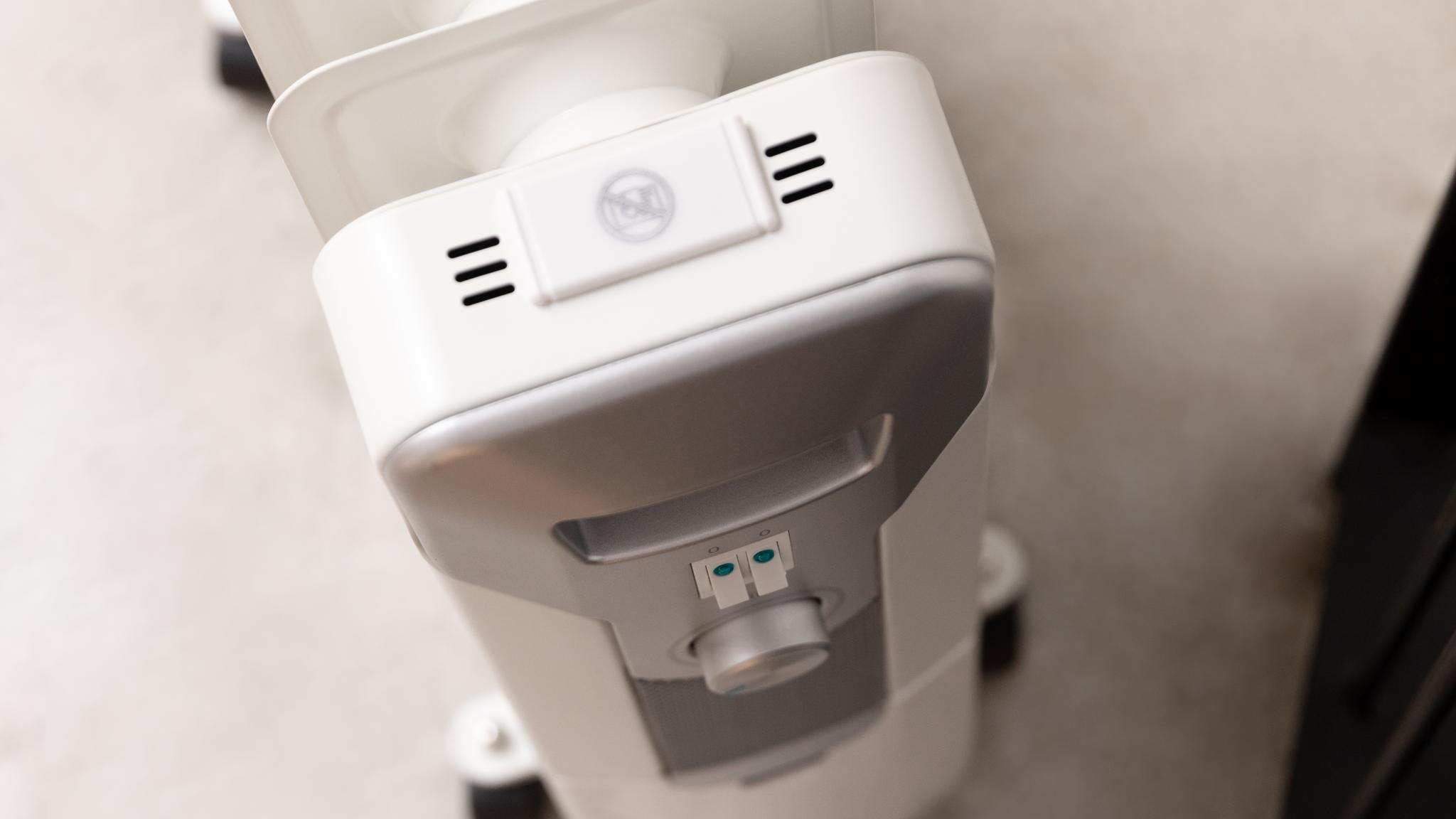 Primer plano de un calefactor eléctrico blanco y plateado. Tiene un panel de control, una perilla y rejillas.