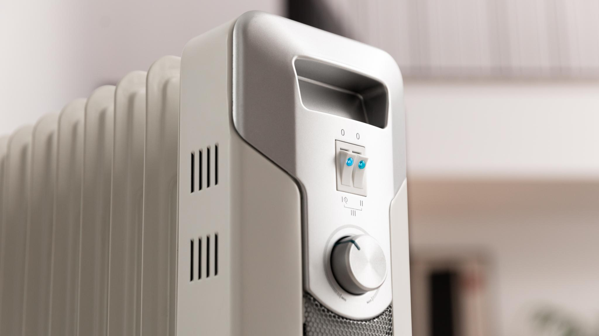 Primer plano de un radiador eléctrico blanco. Tiene un panel de control con interruptores y un dial. El fondo está borroso.