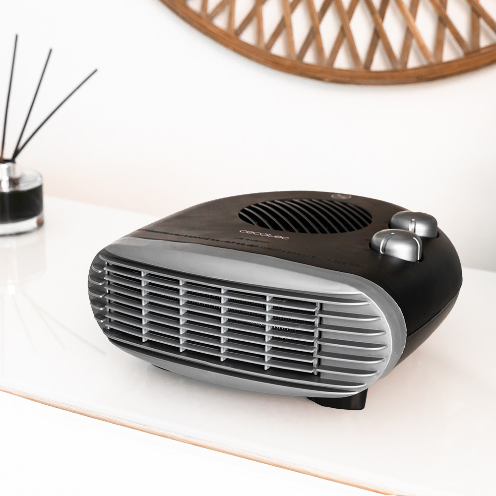 Calentador eléctrico negro y plateado sobre una superficie blanca. Un difusor y una decoración de madera son visibles en el fondo.