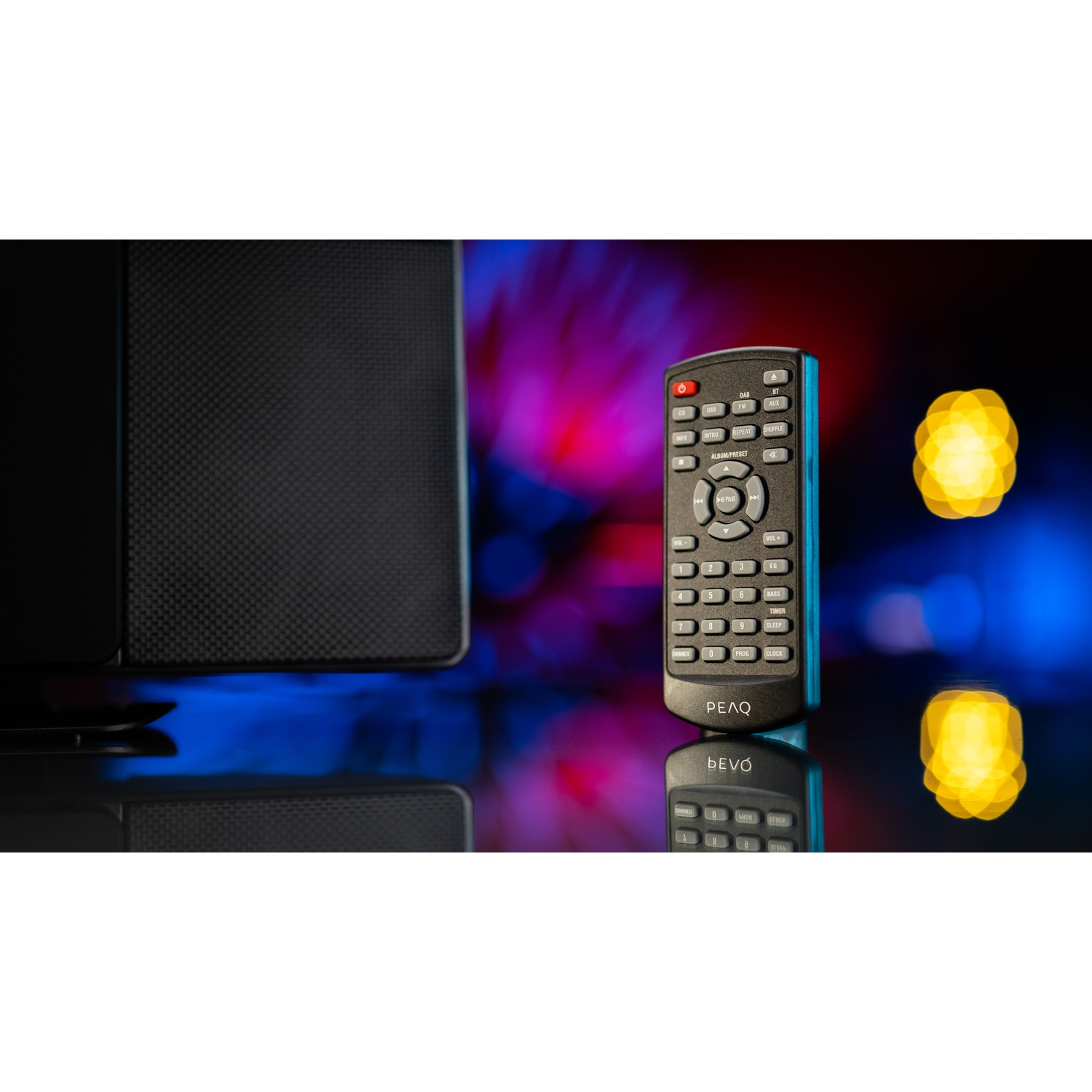 Un telecomando nero con bordi blu è posto davanti a un altoparlante. Lo sfondo ha luci bokeh. Il telecomando si riflette.