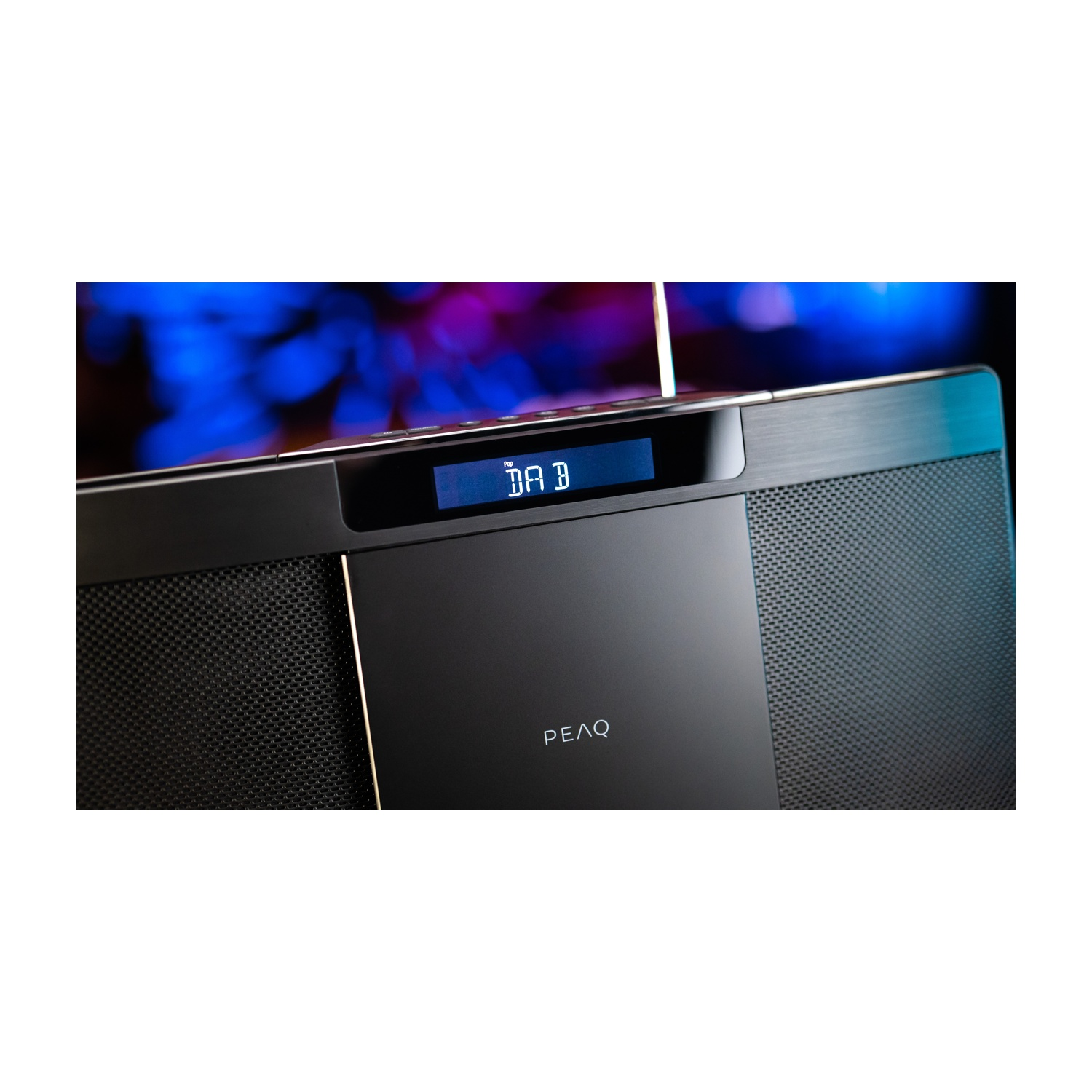 Radio nera con display digitale 'DAB B'. Il marchio 'PEAQ' è sotto. Lo sfondo è sfocato blu e viola.