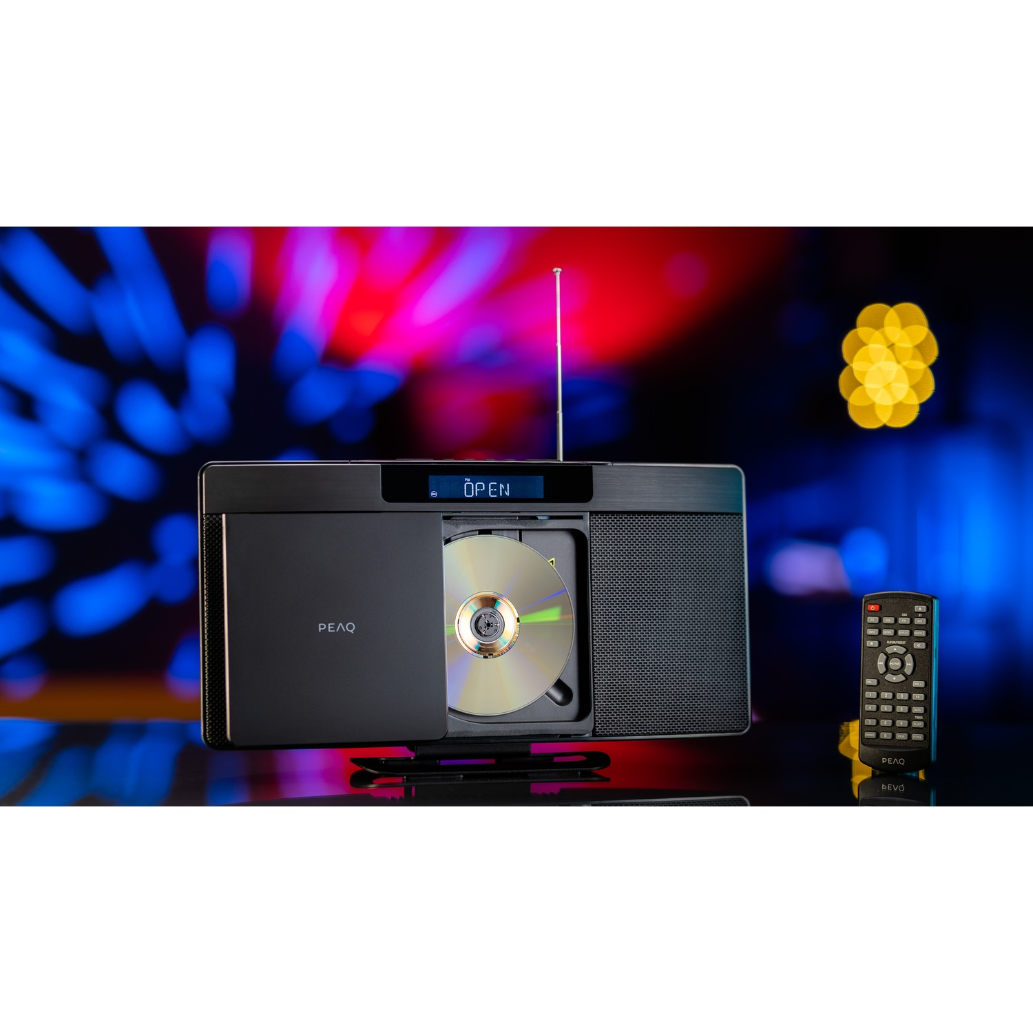 Stereo nero con vassoio CD aperto, antenna e telecomando. Lo sfondo presenta luci bokeh gialle e blu. La parola OPEN è sullo schermo.