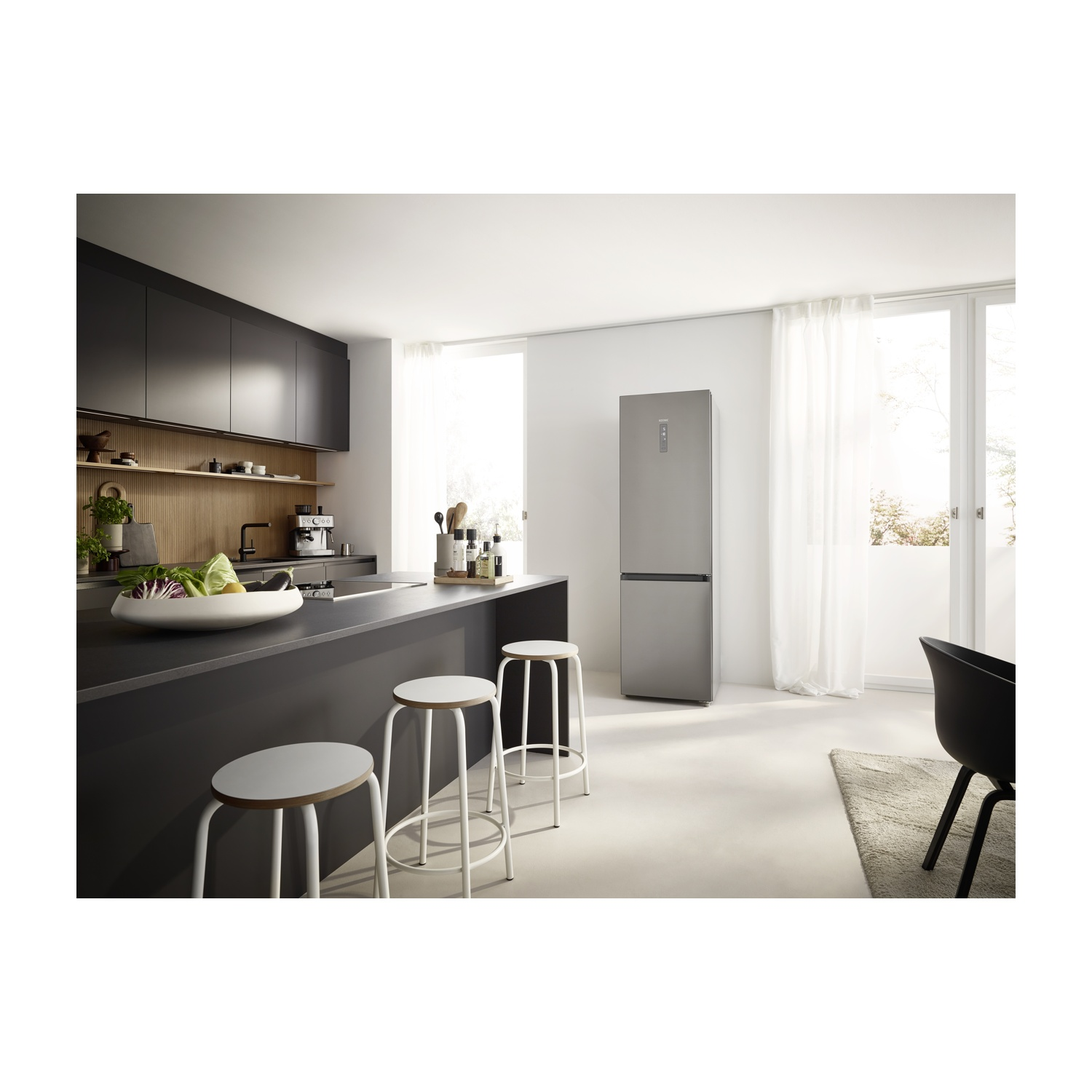 Cucina moderna con frigorifero, isola e sgabelli. Verdure in una ciotola e una sedia nera con tappeto visibili.