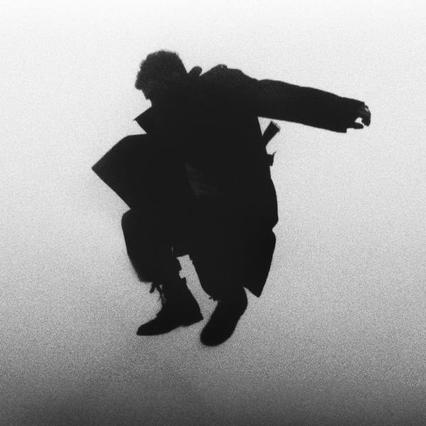 Silhouette einer springenden Person, die einen langen Mantel und Stiefel trägt, vor einem hellen, leicht körnigen Hintergrund.