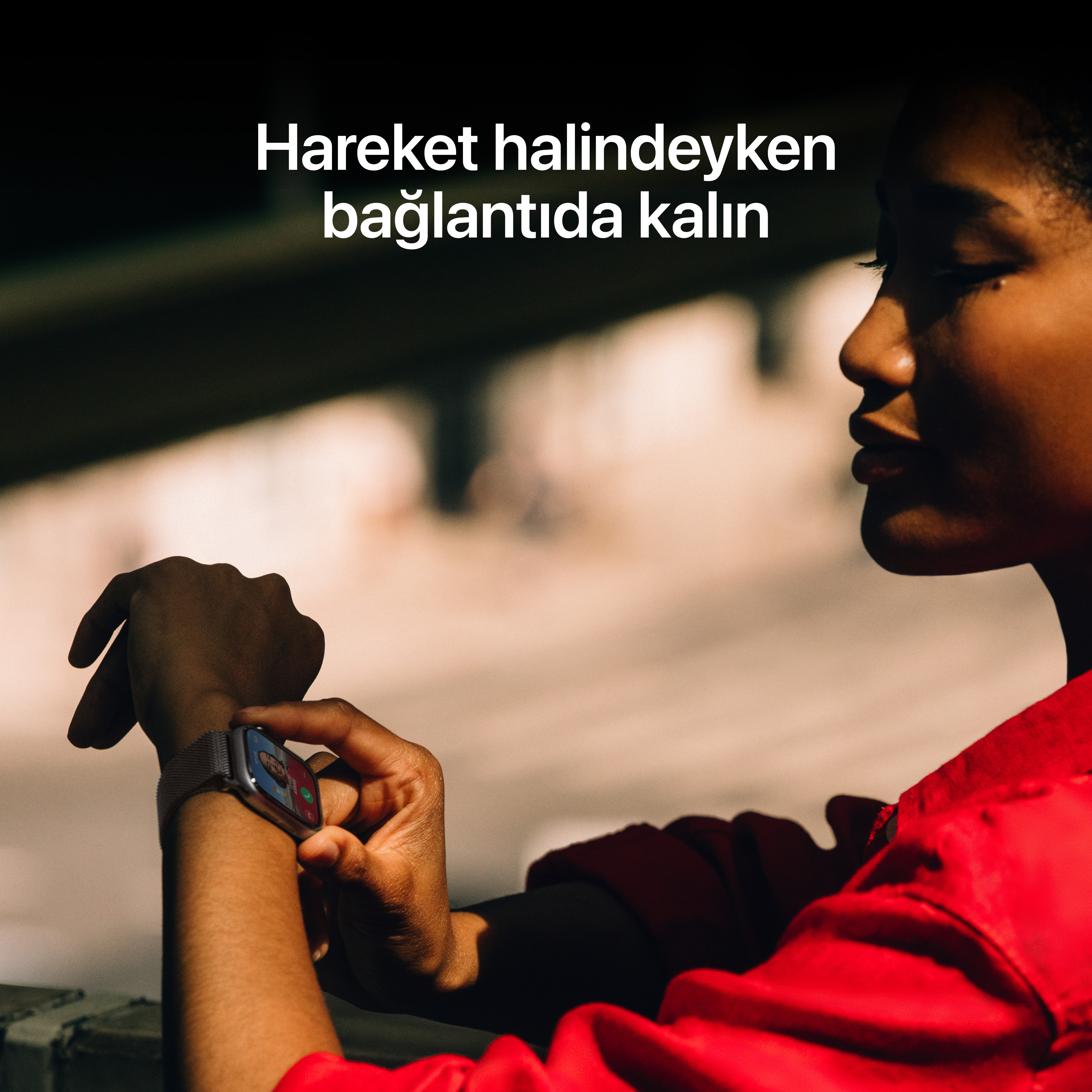 Kırmızı gömlek giyen bir kişi akıllı saatine bakıyor. Türkçe metin: 'Hareket halindeyken bağlantıda kalın'.