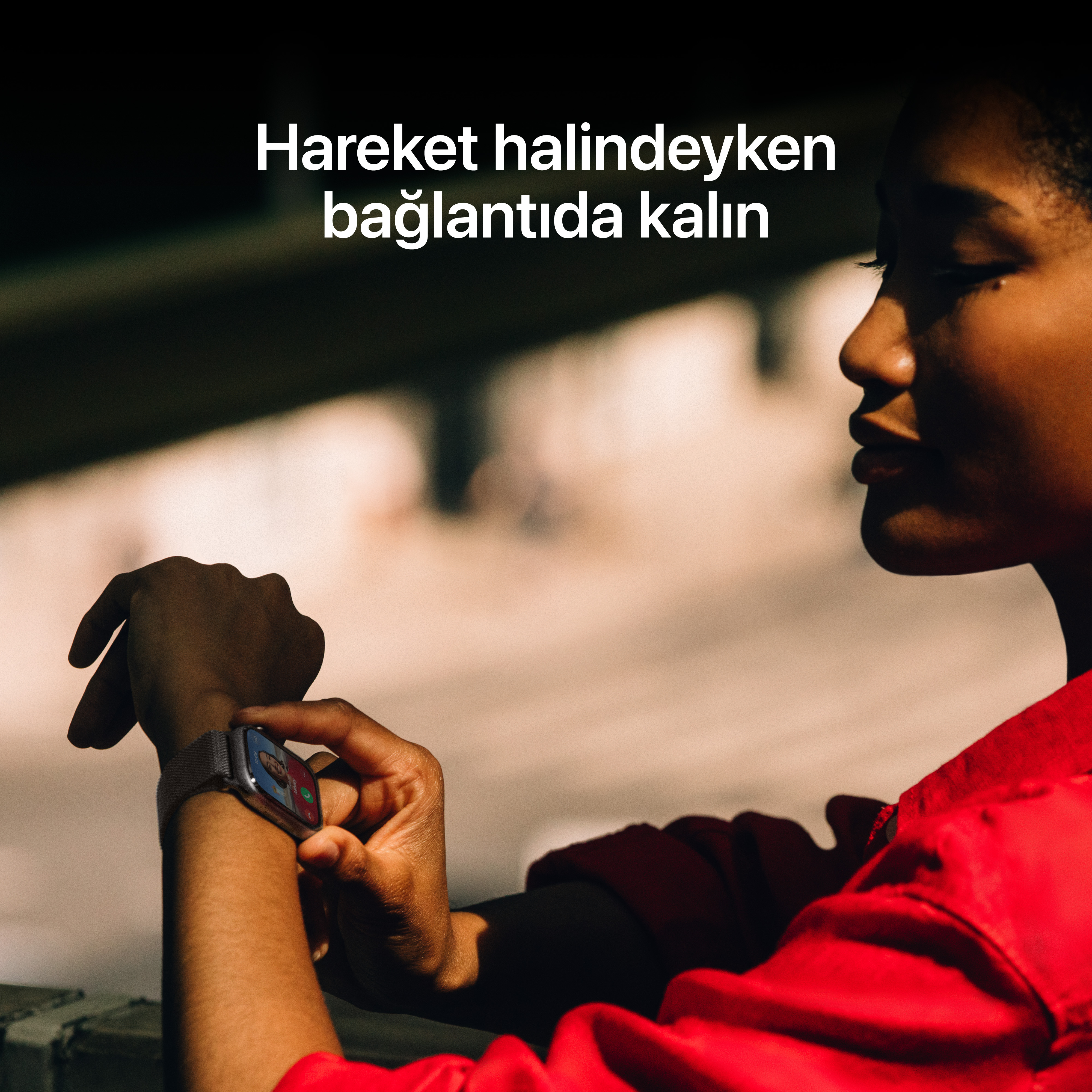 Kırmızı gömlek giyen bir kişi akıllı saatine bakıyor. Saat, bir görüntülü görüşme gösteriyor. Metin Türkçe.