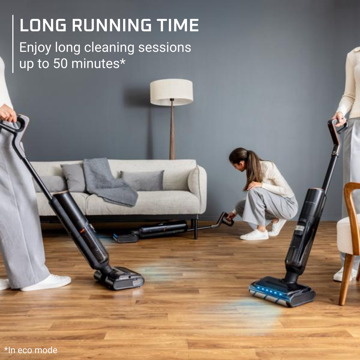 Three people vacuuming a living room. Two use upright vacuums, one is on the floor. A sofa and lamp are in the background.