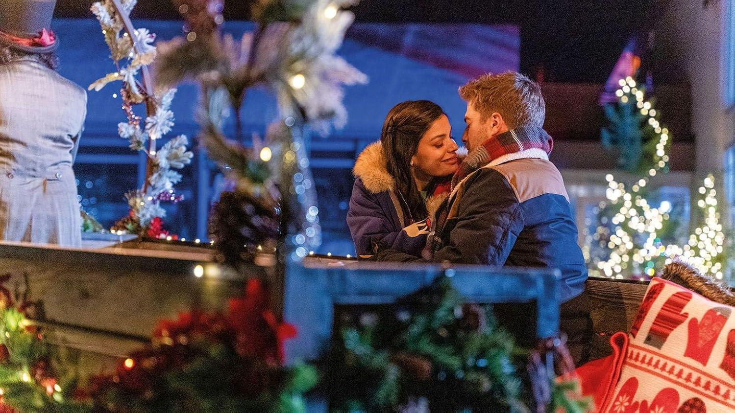 Ein Paar umarmt sich in der Nähe von Weihnachtsdekorationen. Ein Mann und eine Frau stehen sich gegenüber, im Hintergrund sind Lichterketten und Bäume zu sehen.