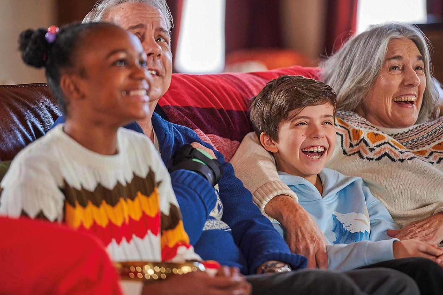 Eine mehrgenerationale Gruppe lacht gemeinsam auf einem Sofa. Ein Kind und eine ältere Frau lächeln breit.