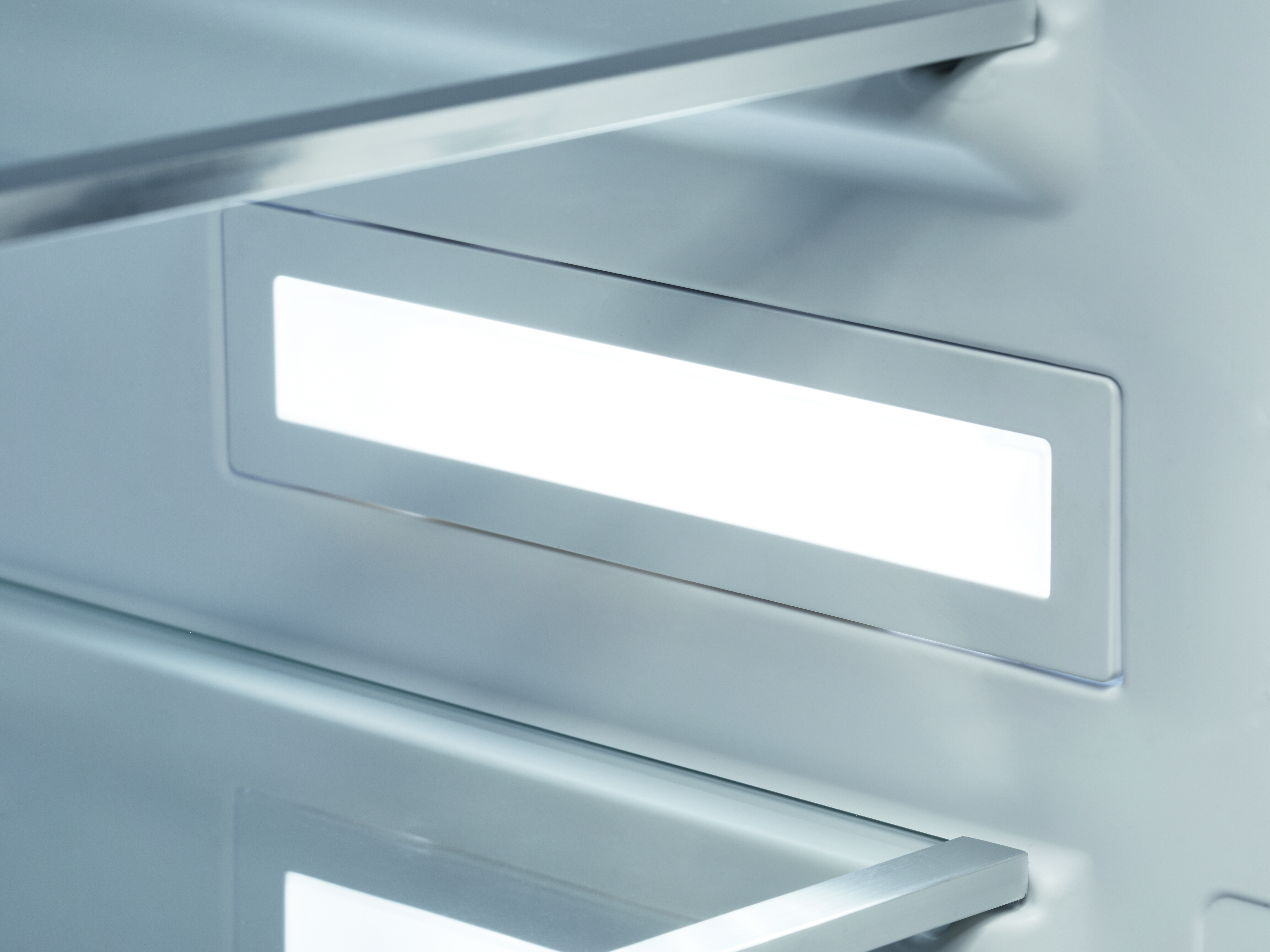 Gros plan d'un éclairage rectangulaire lumineux à l'intérieur d'un réfrigérateur. Étagères et cadre métallique visibles.