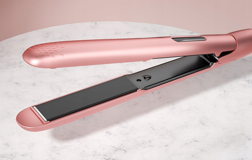 Prostownica w kolorze różowego złota leży otwarta na marmurowej powierzchni. Żelazko ma czarne płytki i jest gotowe do użycia.