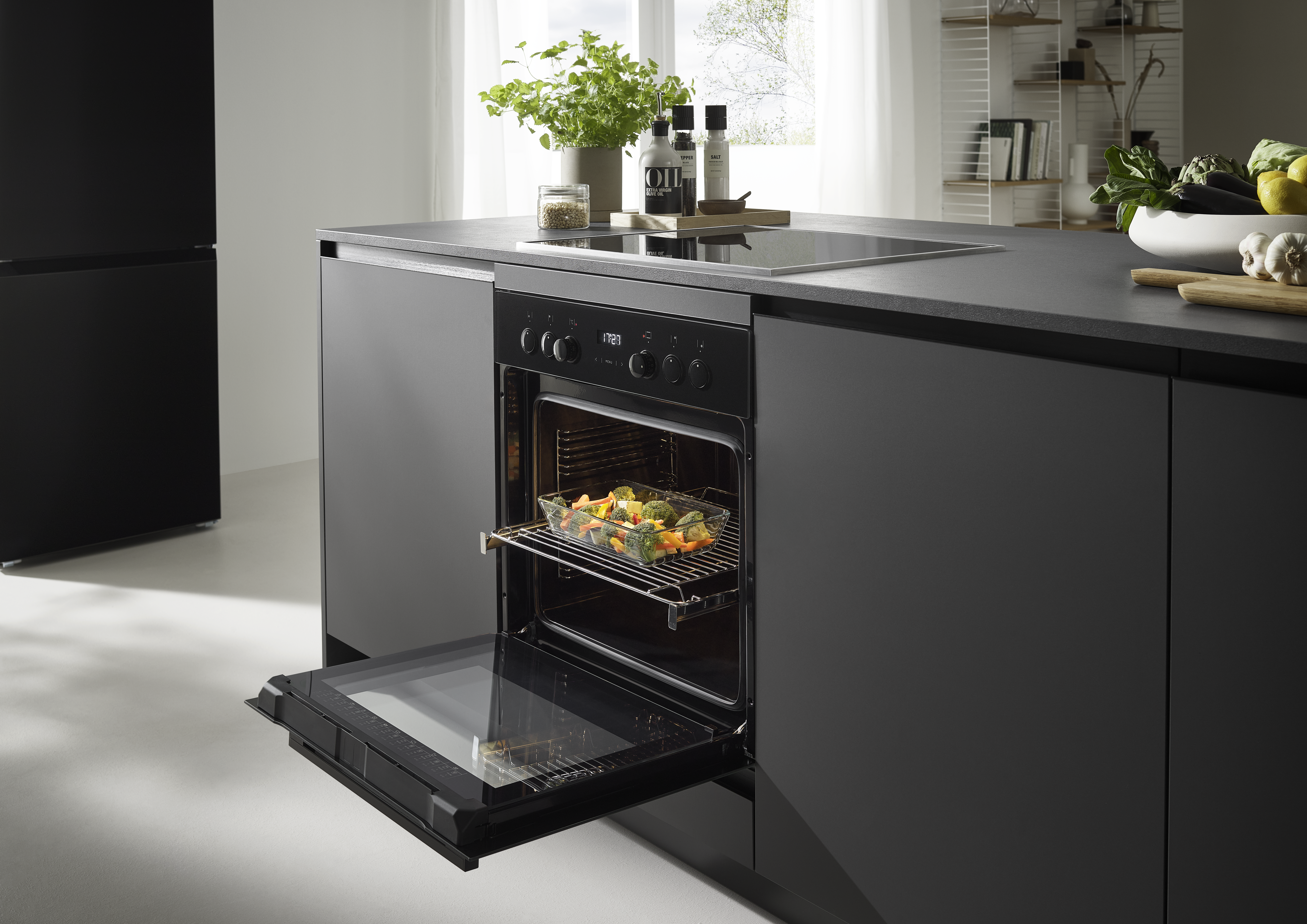 Moderne Küche mit offenem Backofen mit Gemüse. Die Szene umfasst eine dunkle Arbeitsplatte, Schränke und verschiedene Küchenartikel.