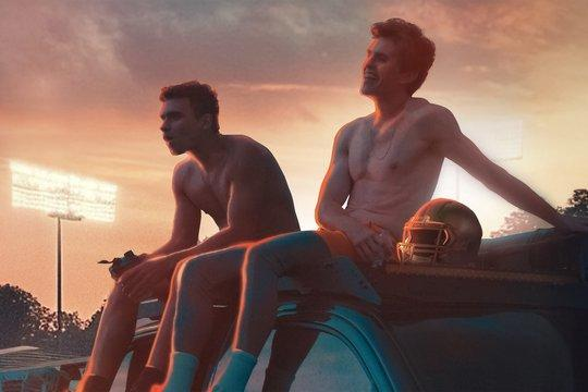 Zwei Männer ohne Hemd sitzen auf einem Auto, ein Footballhelm liegt daneben. Der Himmel ist sonnenfarben, im Hintergrund ist ein Stadionlicht zu sehen.