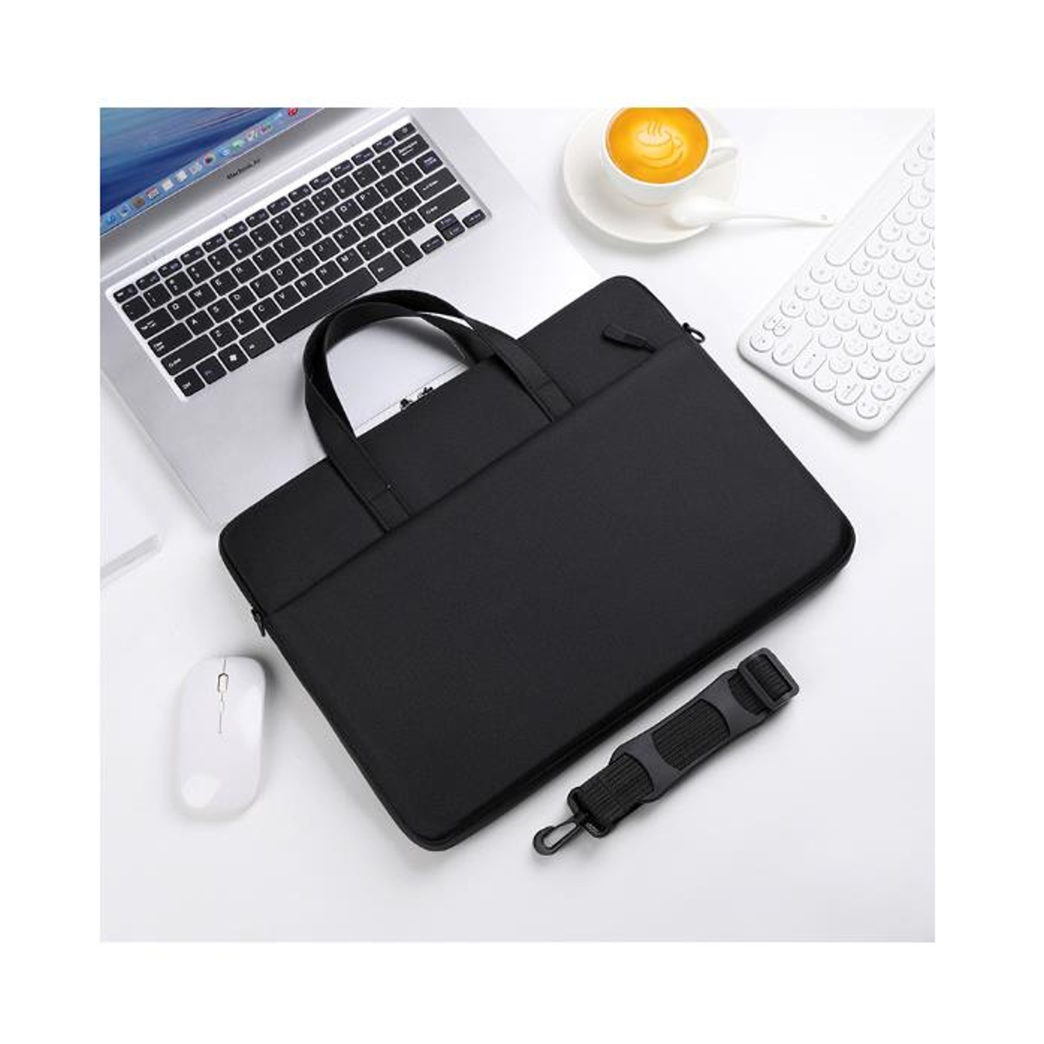 Un laptop, una borsa nera per laptop, un mouse bianco, una tazza di caffè e una tastiera bianca sono su una superficie bianca.