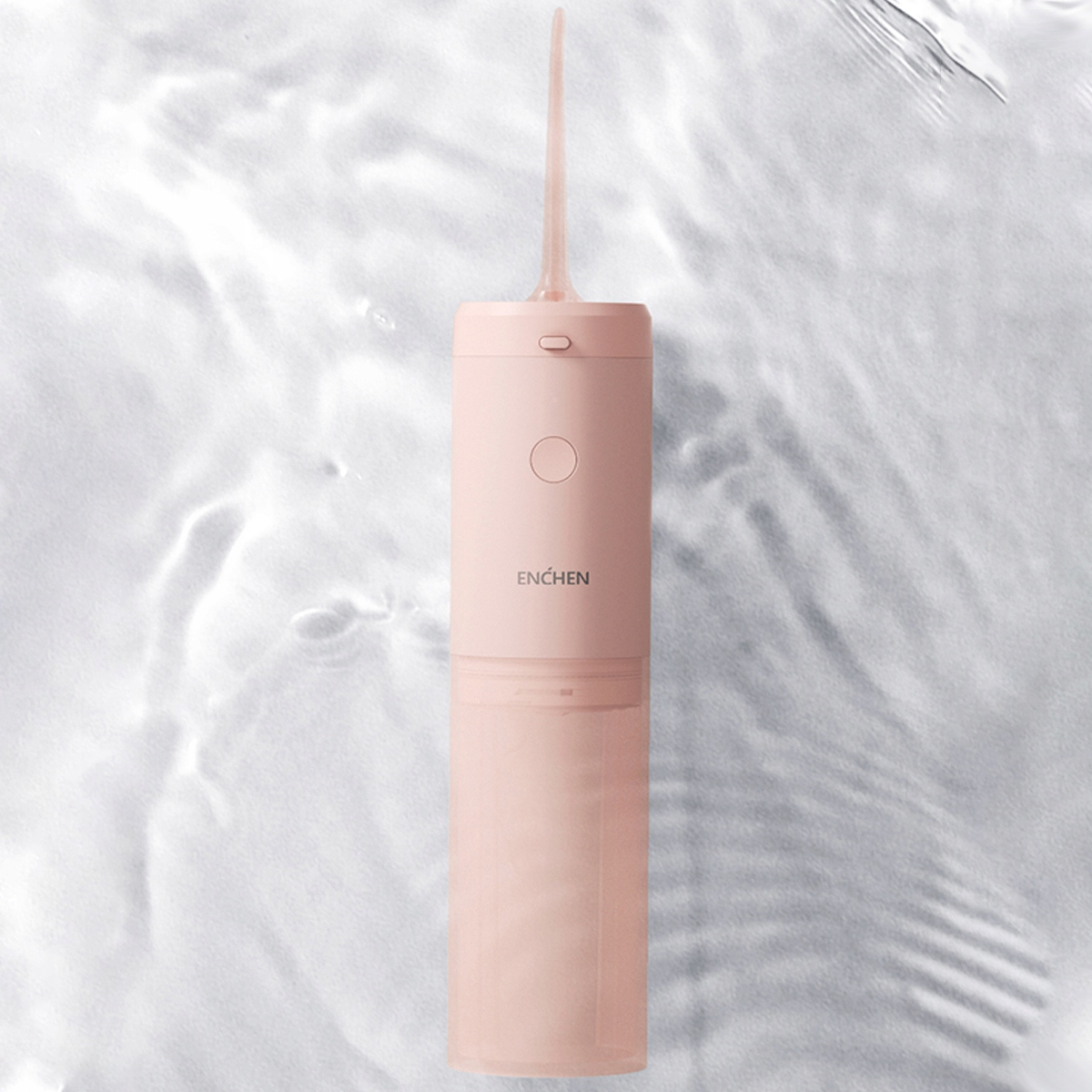 Różowy irygator do jamy ustnej z dyszą, na falistym, wodnym tle. Marka 'Enchen' jest wydrukowana.