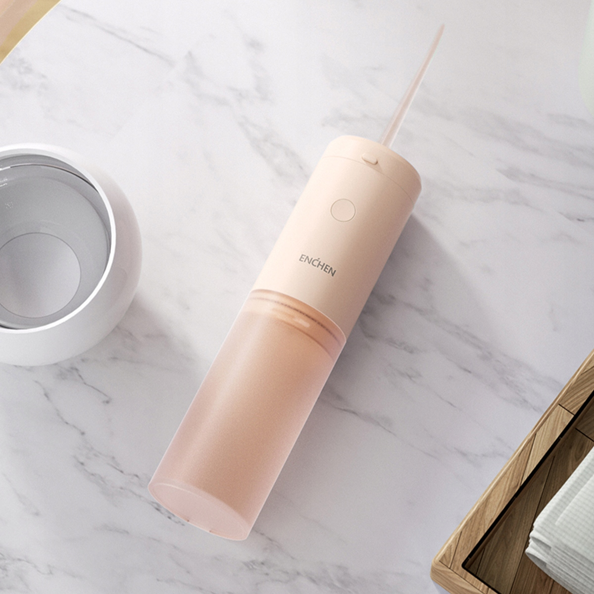 Różowy irygator i biały wazon na marmurowej powierzchni. Irygator ma długą końcówkę. Drewniana taca po prawej.