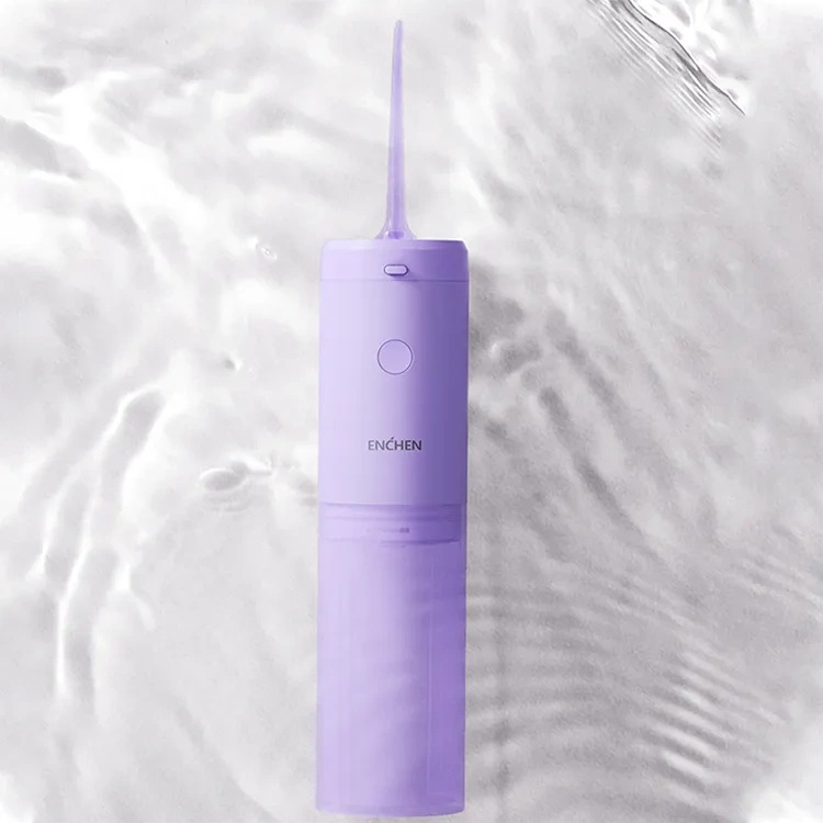 Liliowy irygator do zębów Enchen stoi na tle pofałdowanej wody. Ma długą dyszę i przycisk.