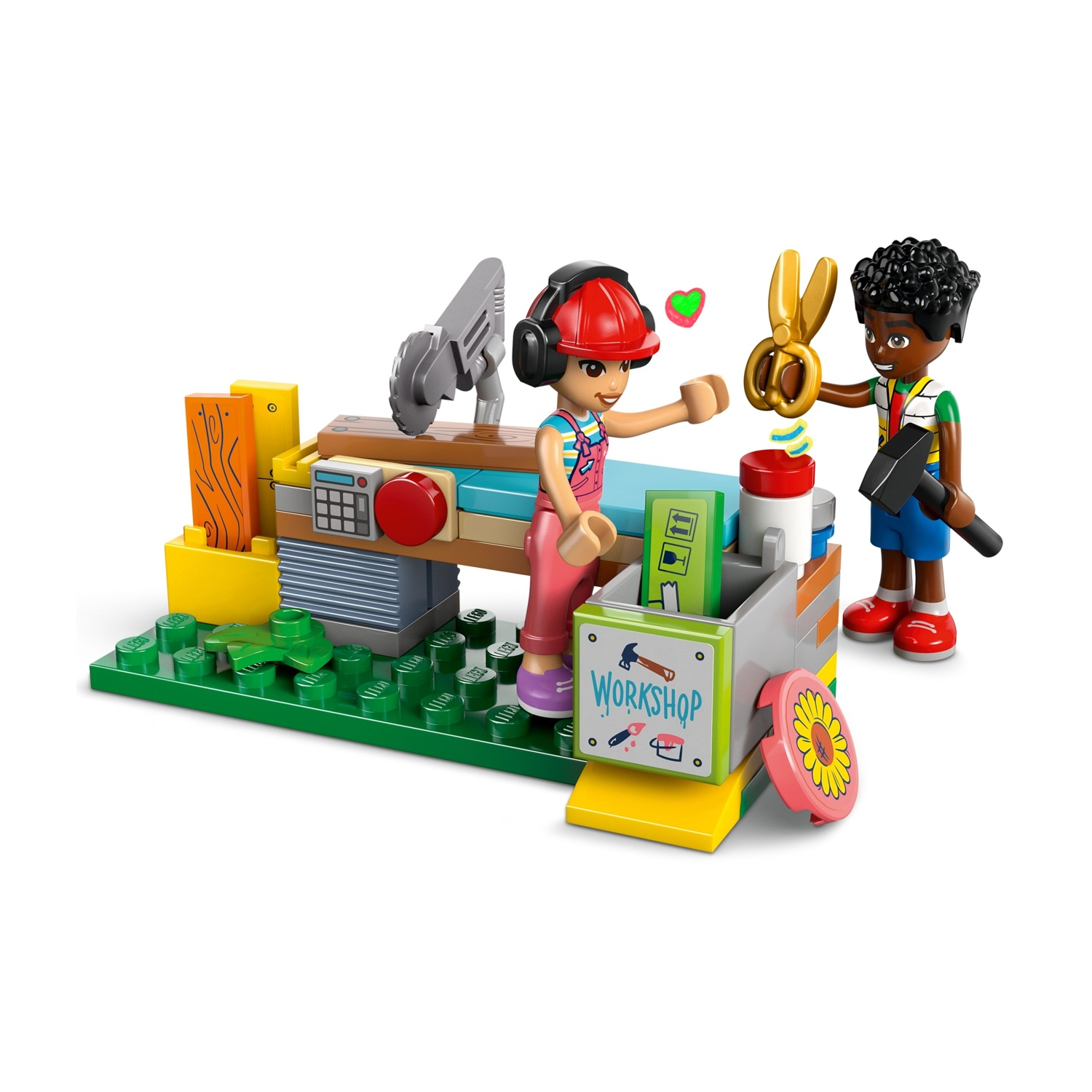 Scena del laboratorio Lego. Una ragazza con casco rosso e un ragazzo con un martello. Forbici, legno e base verde sono visibili.