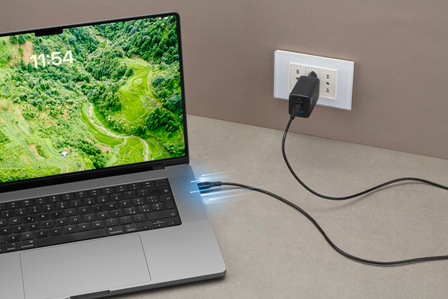 Ordenador portátil con pantalla de paisaje, cargando con cable negro a enchufe y adaptador. La hora es 11:54.
