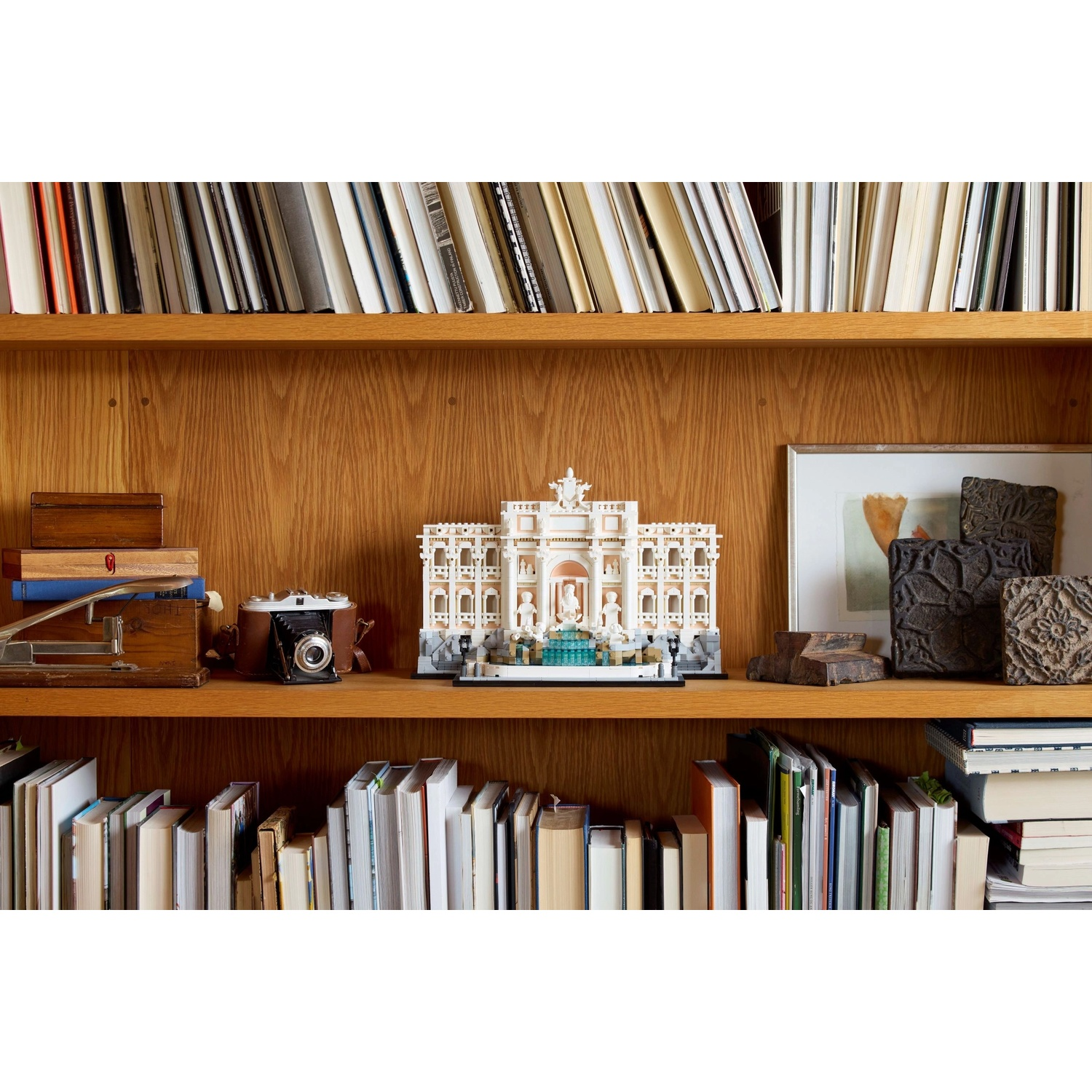 Una libreria in legno con libri e oggetti decorativi. Una fontana giocattolo è sullo scaffale. Una fotocamera, opere d'arte e altri oggetti sono visibili.
