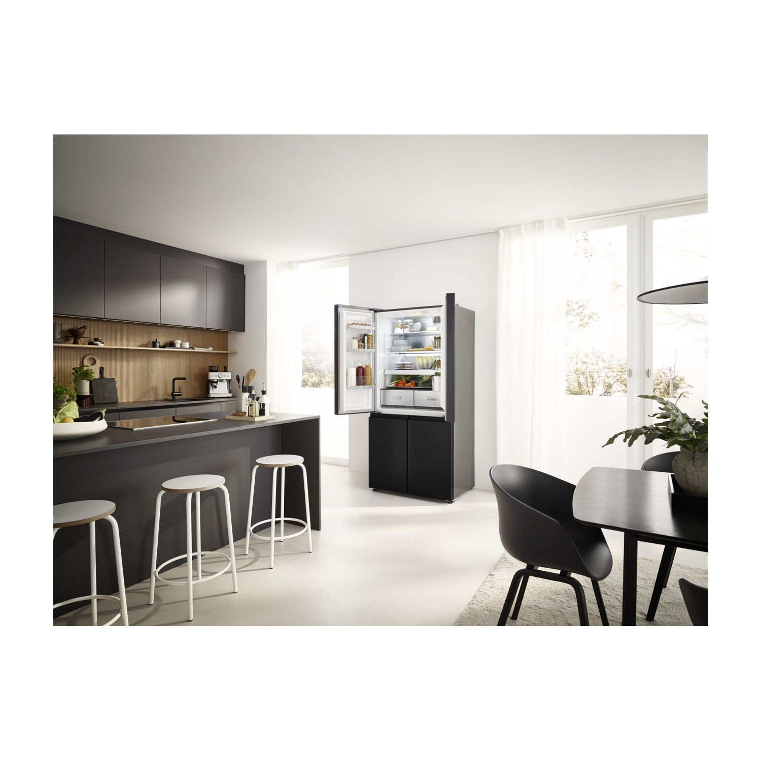 Cucina moderna con frigorifero aperto, isola con sgabelli e zona pranzo. Mobili e elettrodomestici neri, pareti e pavimento bianchi.
