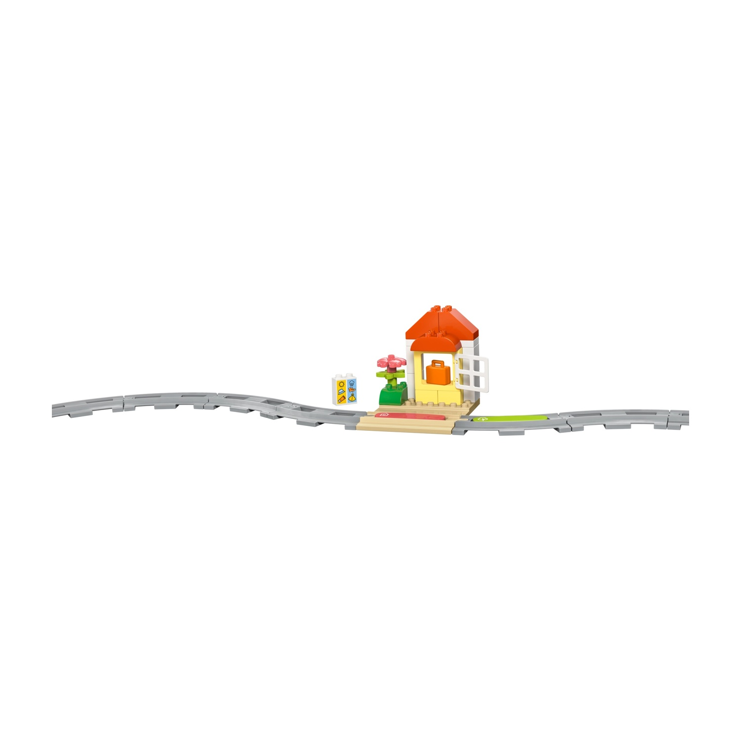Una stazione ferroviaria Lego con binari. Ha un tetto arancione, pareti gialle e un cartello. Ci sono fiori e una borsa arancione.
