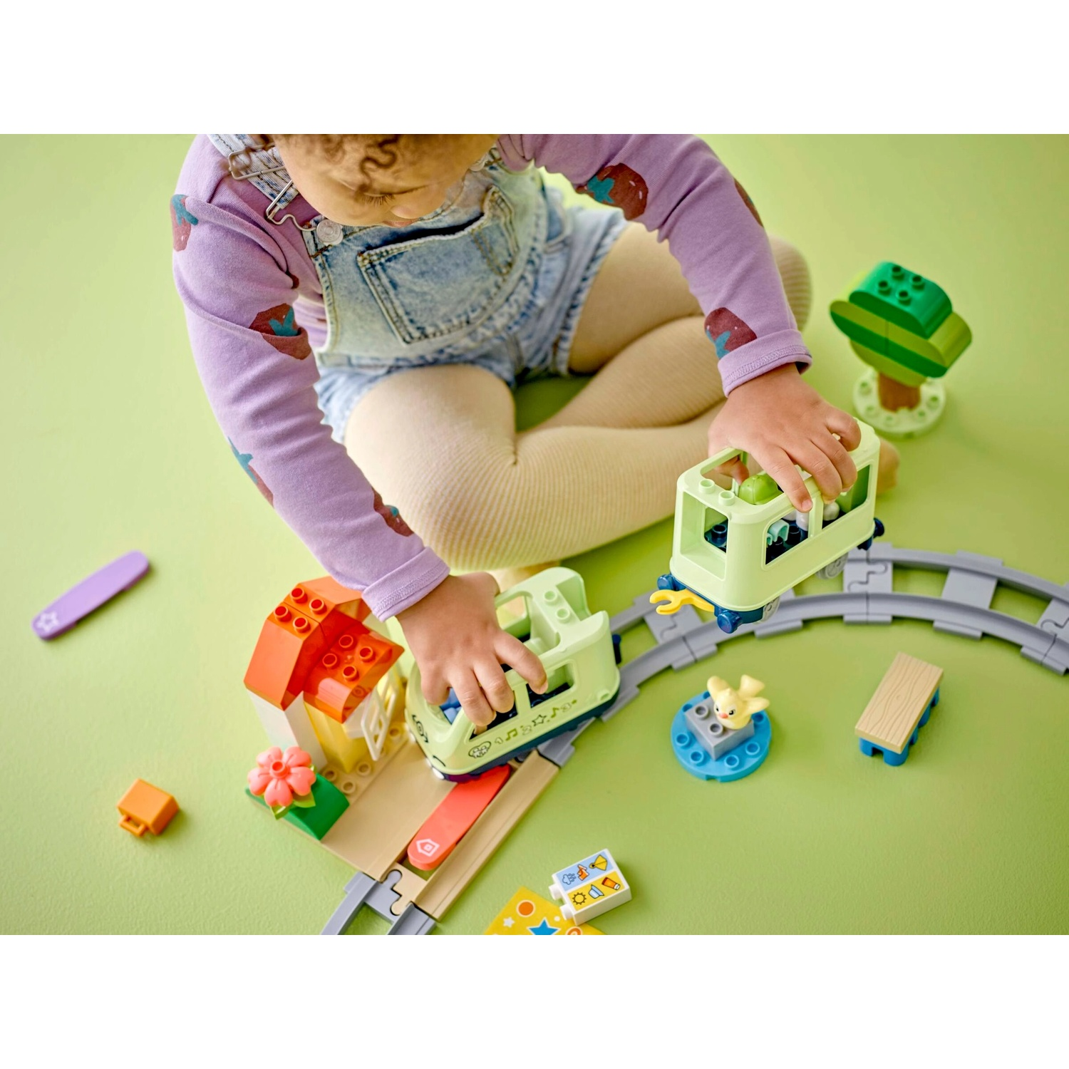 Un bambino gioca con un trenino giocattolo. Il set include un treno, binari, una casa, un albero e altri blocchi colorati.