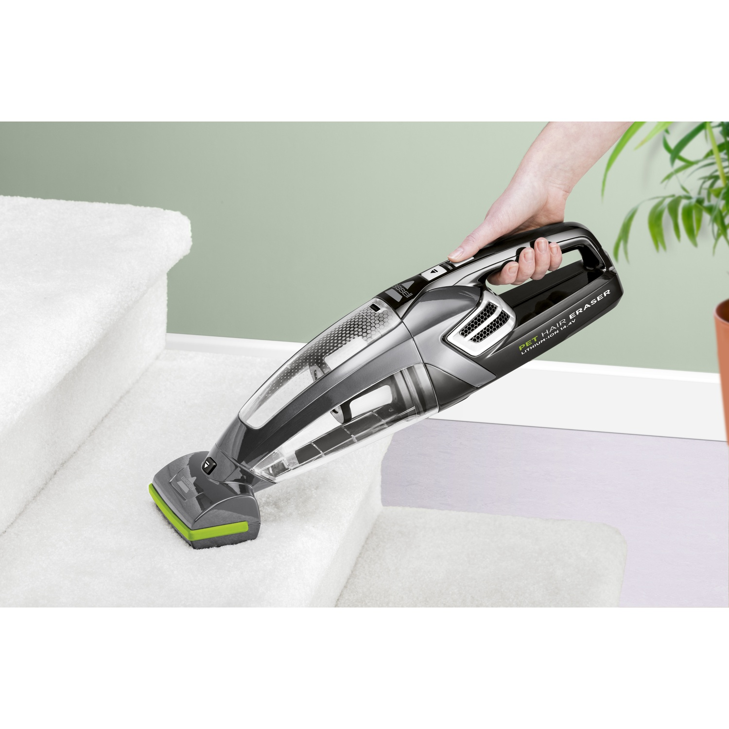 Una mano tiene un aspirapolvere Bissell Pet Hair Eraser nero e grigio su scale rivestite di moquette bianca. Accenti verdi sull'aspirapolvere.