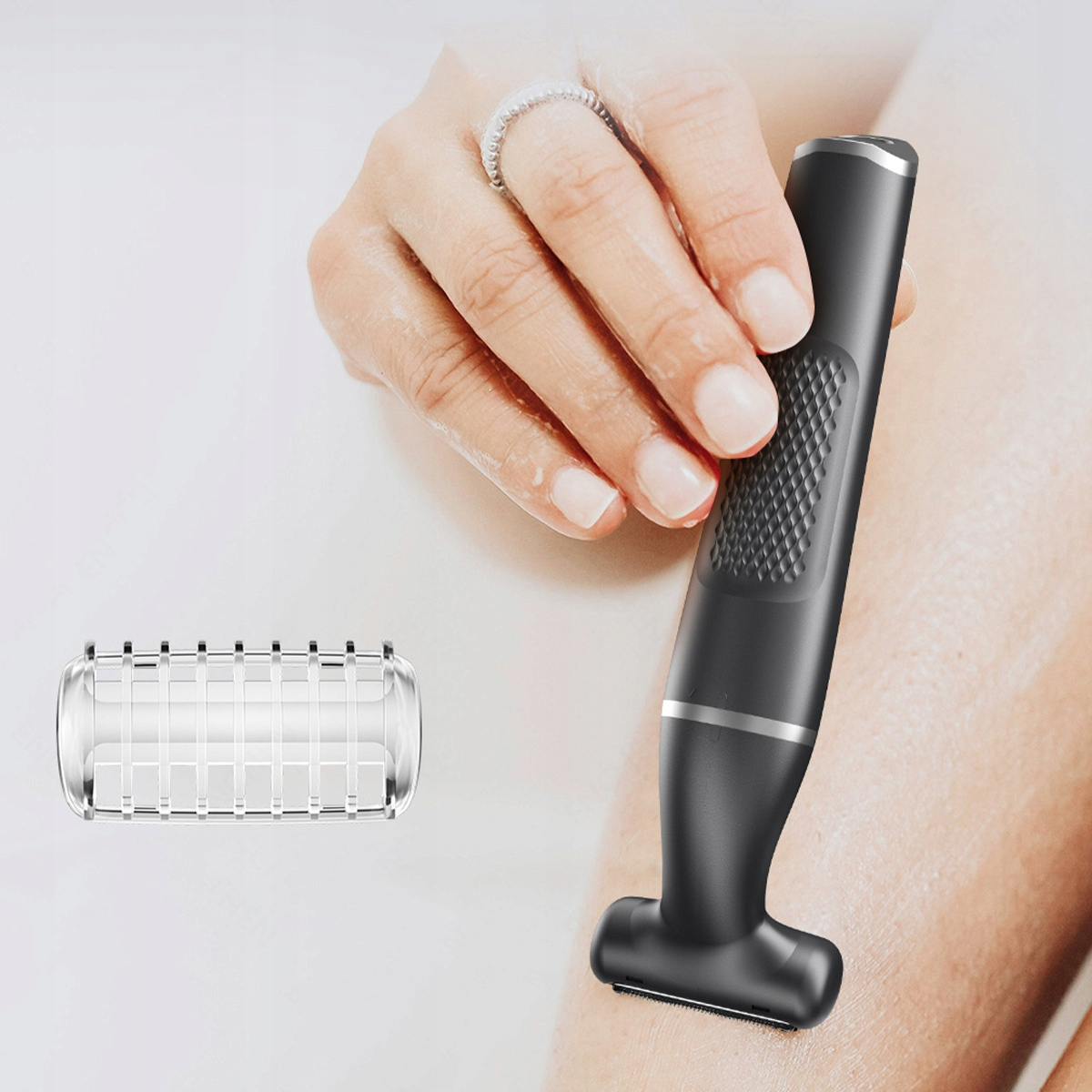 Dłoń z pierścionkiem trzyma czarną golarkę przy nodze. Osobna głowica golarki jest po lewej stronie.