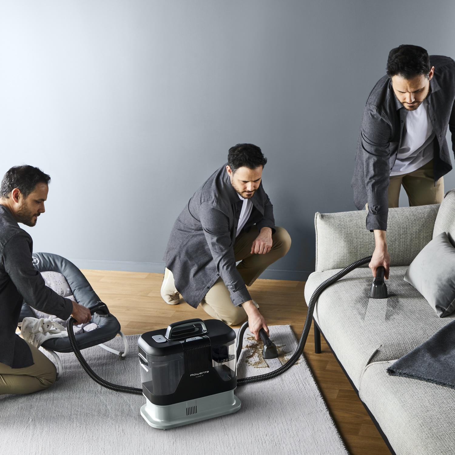 Trois hommes nettoient avec un nettoyeur Rowenta : un transat, un tapis et un canapé. Mur et tapis gris en arrière-plan.