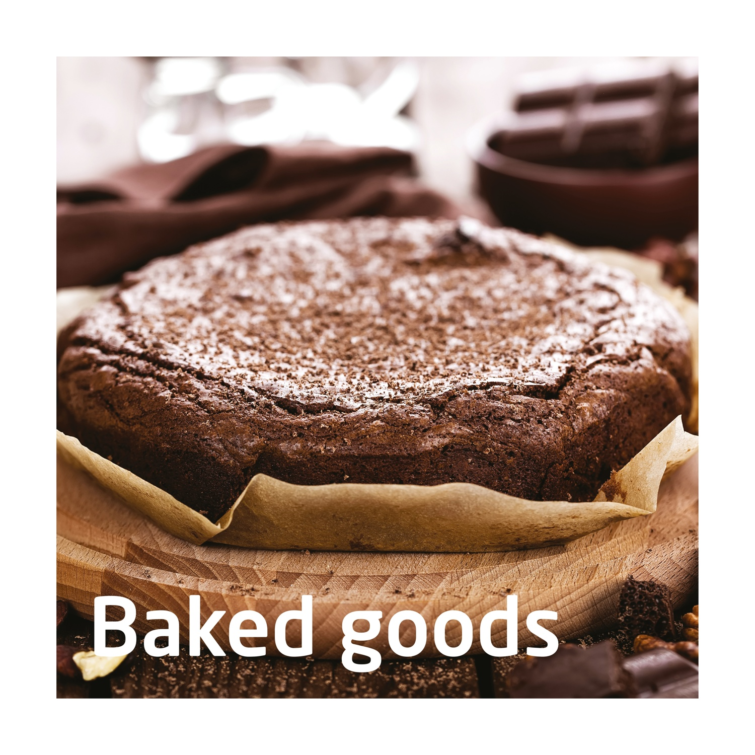 Primo piano di una torta al cioccolato su un tagliere di legno. Prodotti da forno marroni con una leggera spolverata di polvere. Barrette di cioccolato e noci circondano la torta.