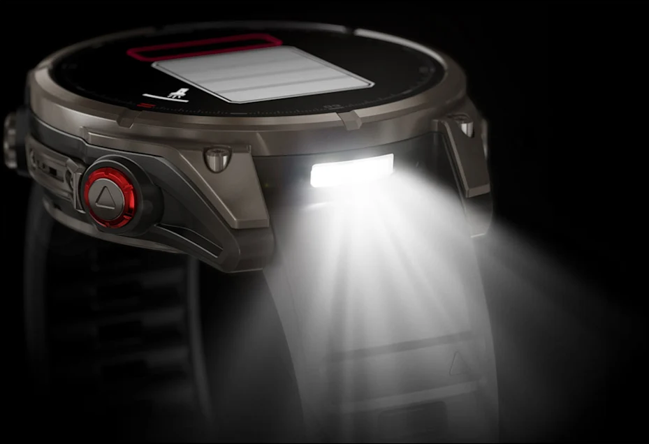 Gros plan d'une montre intelligente avec une lumière vive. Elle a une lunette noire et un bouton rouge. Le fond est sombre.