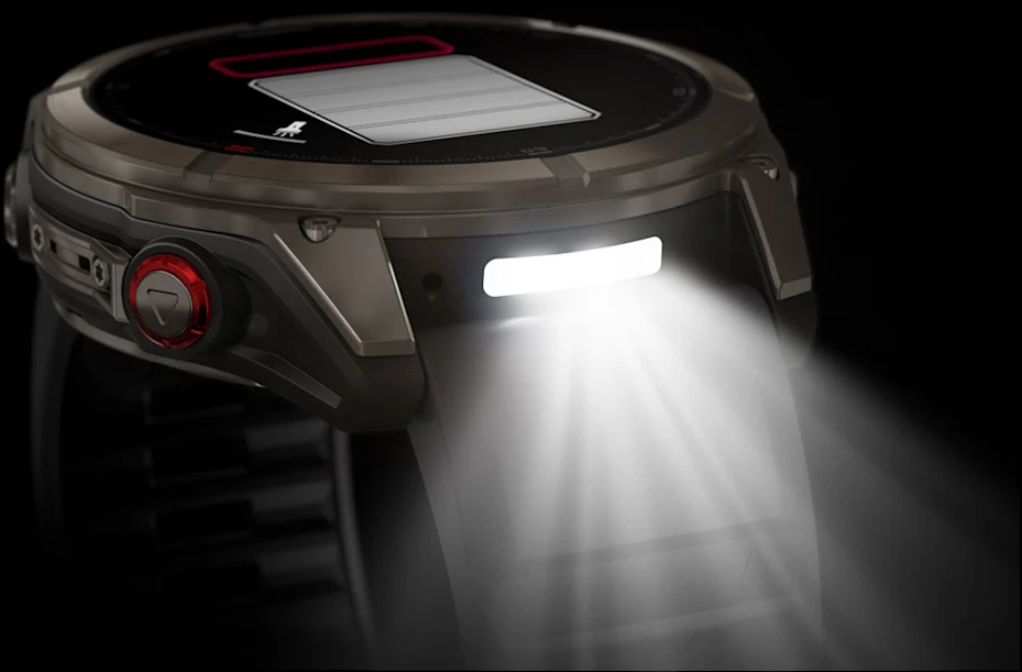 Uno smartwatch scuro con una luce che brilla verso l'esterno. L'orologio è grigio metallizzato con un pulsante rosso. Lo schermo mostra il livello della batteria.