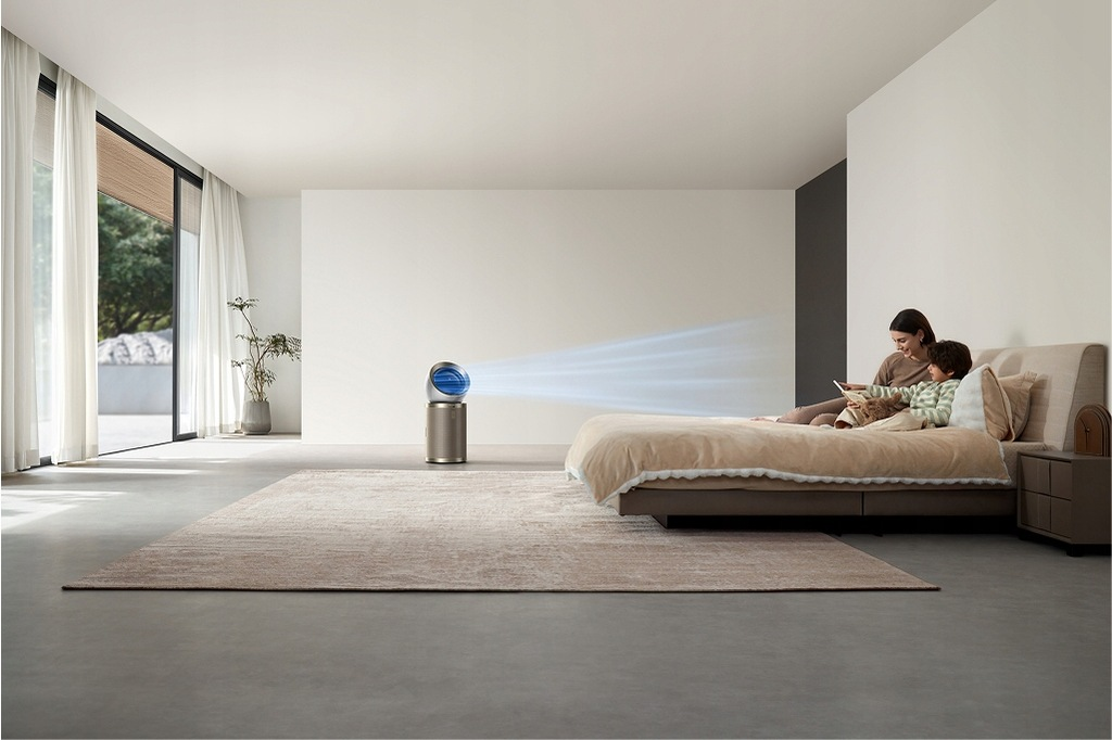 Kobieta i dziecko siedzą na łóżku i czytają. Oczyszczacz powietrza jest na środku. Okno i dywan w tle.