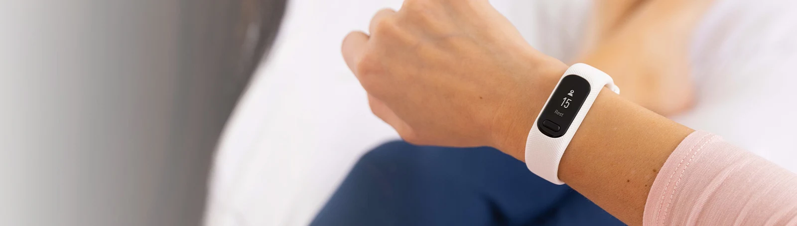 Il polso di una persona con un fitness tracker bianco che mostra i dati del sonno. La persona indossa una camicia rosa.