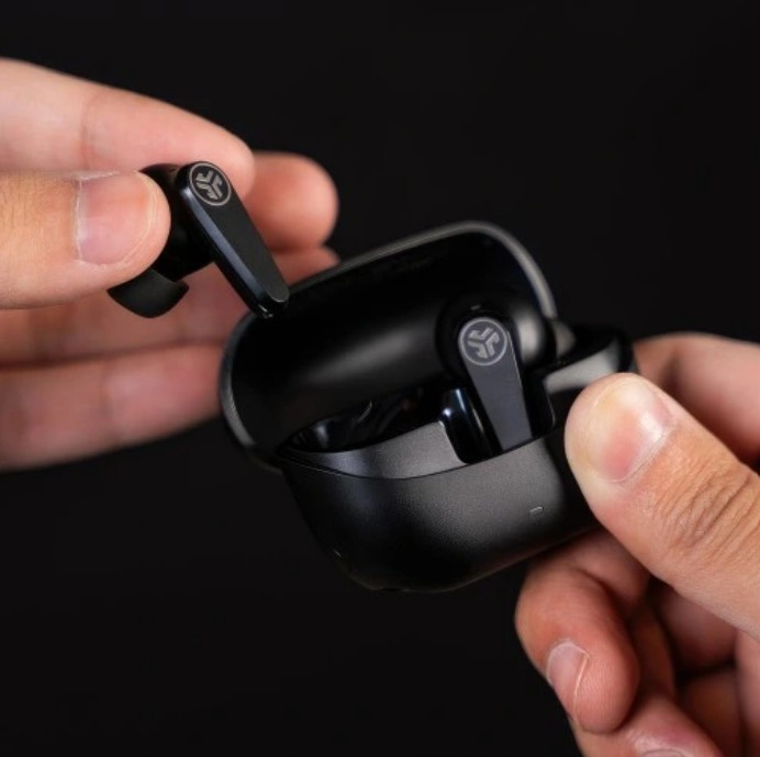 Ręce trzymają czarne bezprzewodowe słuchawki i etui ładujące. Wyjmowanie słuchawki. Czarne tło.