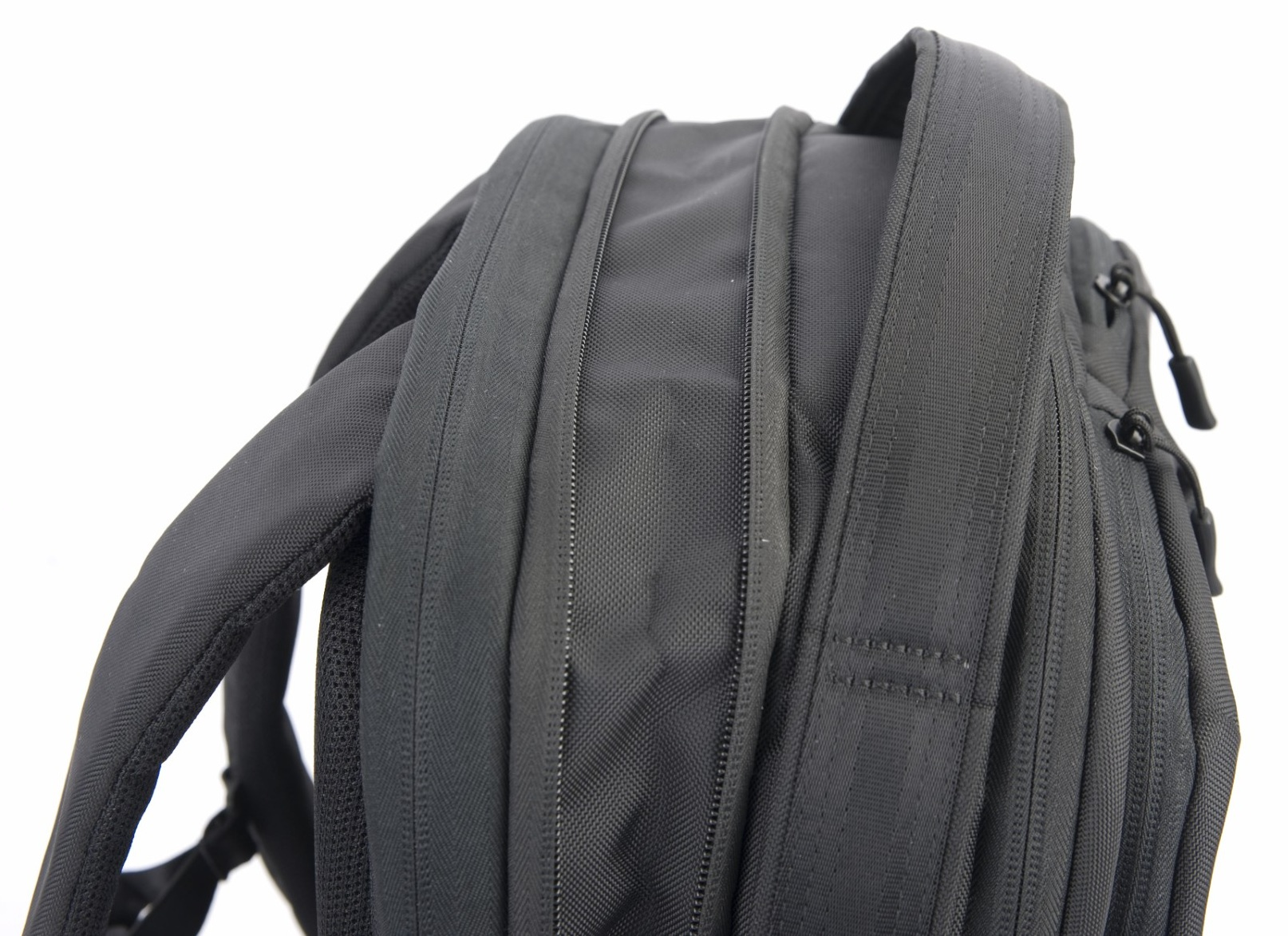 Zbliżenie czarnego plecaka. Obraz pokazuje paski, zamki błyskawiczne i detale materiału na białym tle.