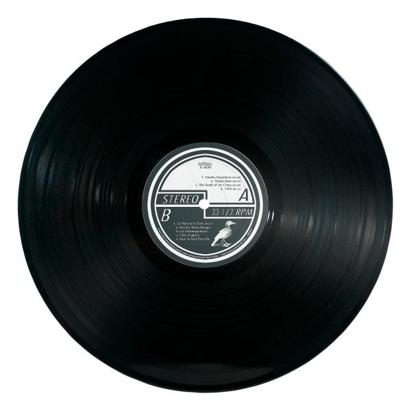 Eine schwarze Schallplatte mit weißem Label. Das Label hat Text und eine Zeichnung eines Vogels. Die Platte ist auf weißem Hintergrund.