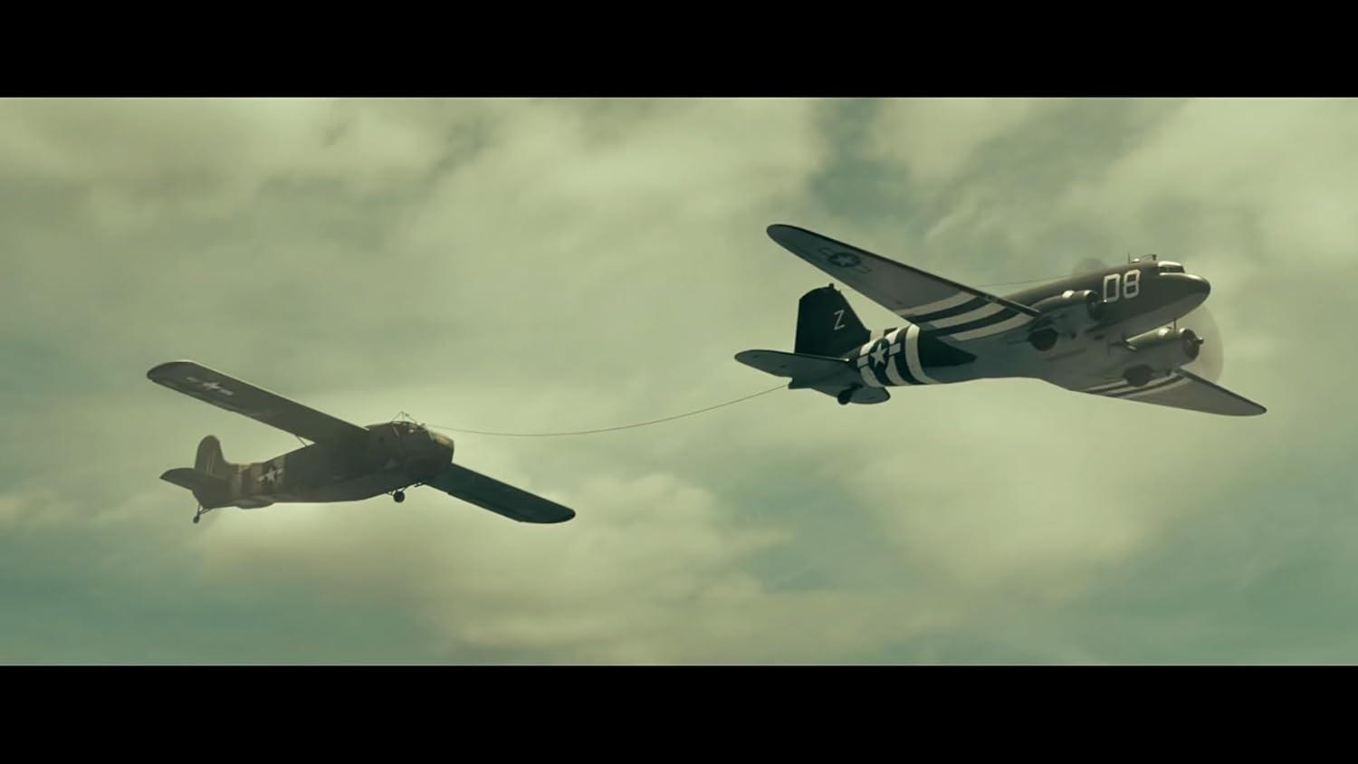 Zwei Militärflugzeuge im Flug, eines schleppt das andere. Wolkenhimmel im Hintergrund. Das führende Flugzeug hat '08' an der Seite.