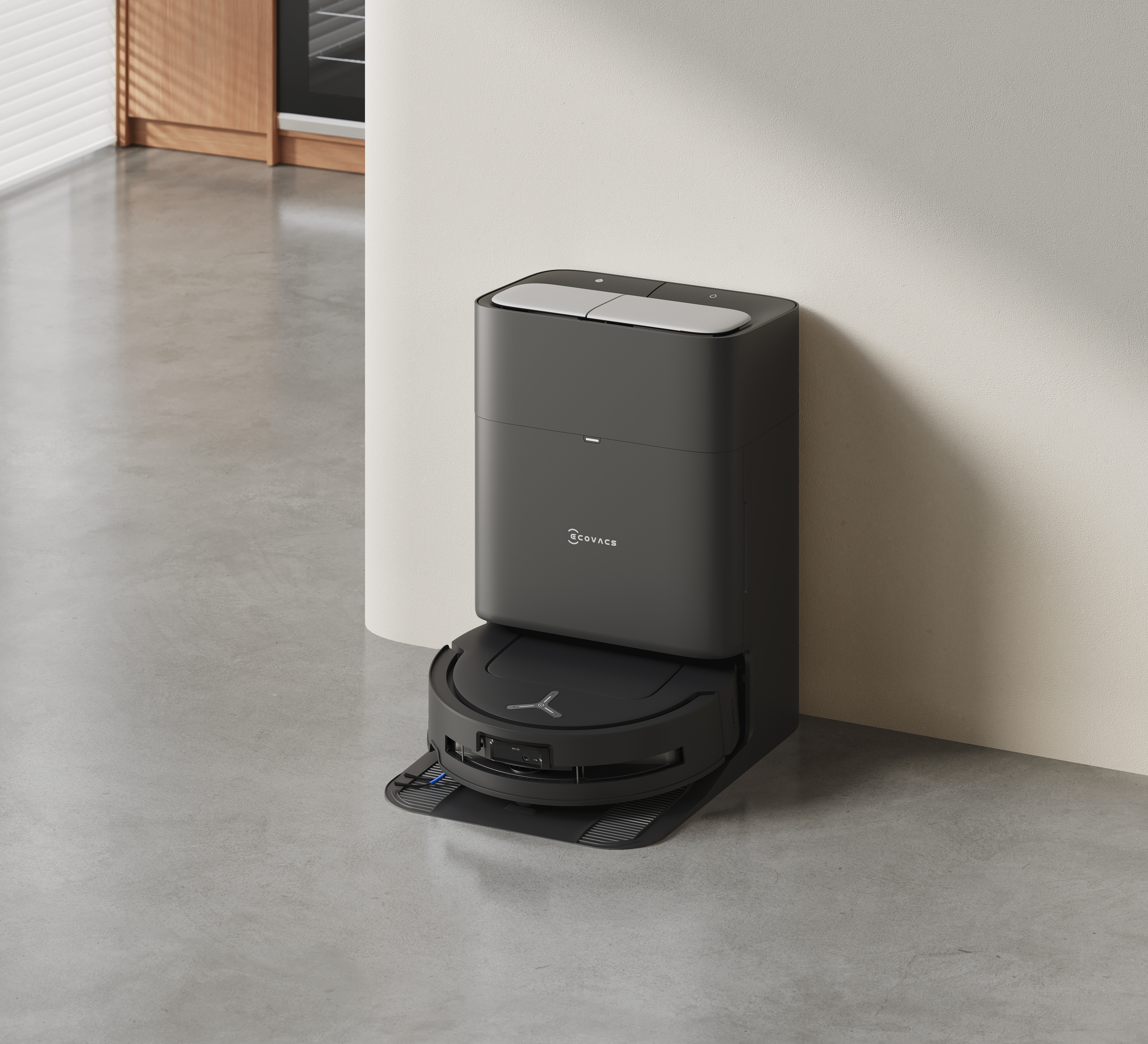 Czarny odkurzacz robot w stacji dokującej na betonowej podłodze, w pobliżu beżowej ściany.