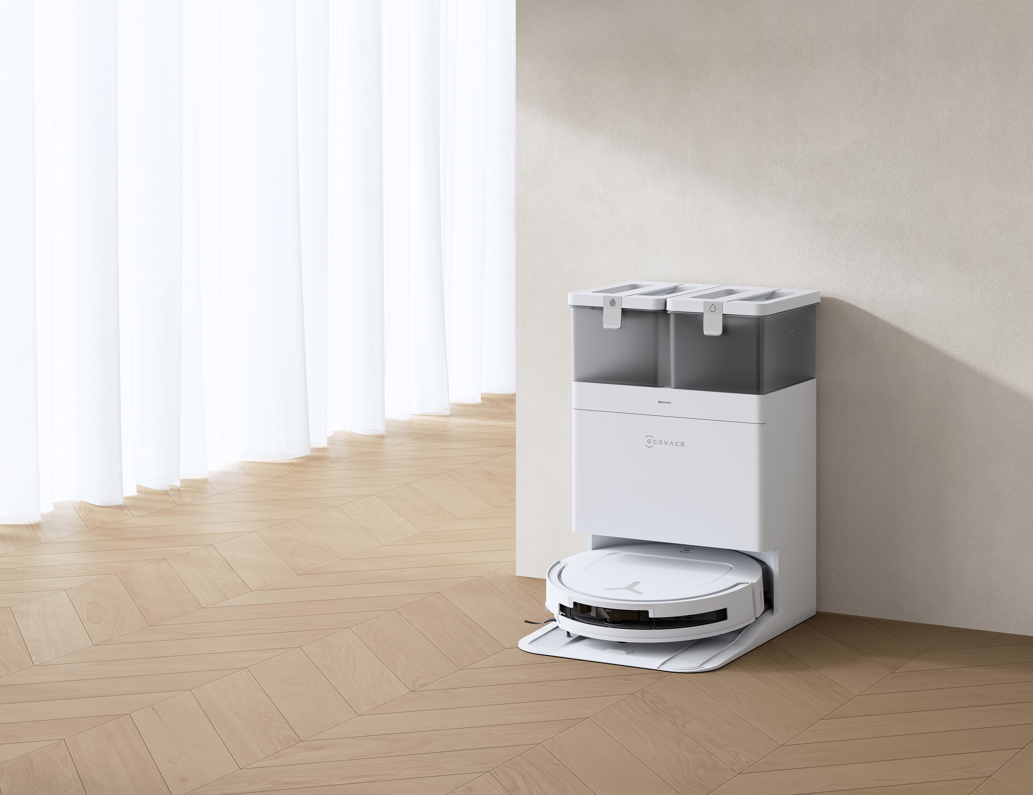 Biały robot odkurzający i stacja ładująca na tle jasnobeżowej ściany, jasnej drewnianej podłogi i białych zasłon.