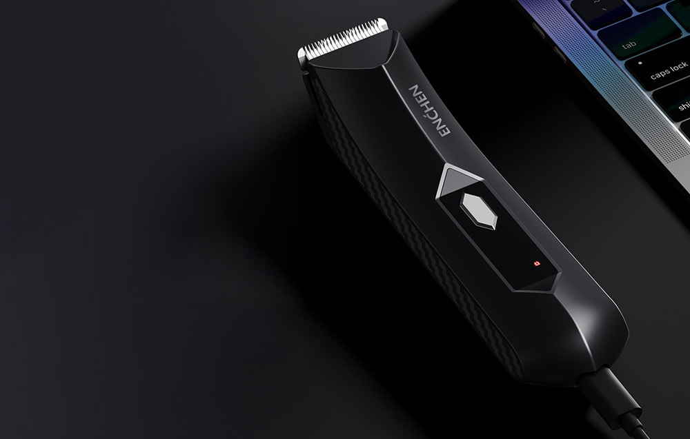 Czarna elektryczna maszynka do włosów na ciemnej powierzchni. W tle widoczny laptop.