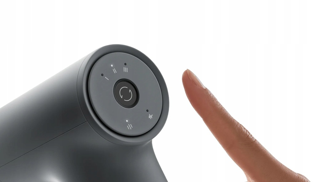 Szare urządzenie z okrągłym panelem sterowania. Palec dotyka panelu. Białe tło.