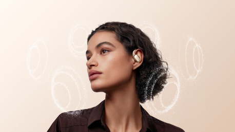 Kobieta w złotych słuchawkach, patrząca w lewo. Białe, okrągłe wzory za nią na jasnobrązowym tle.